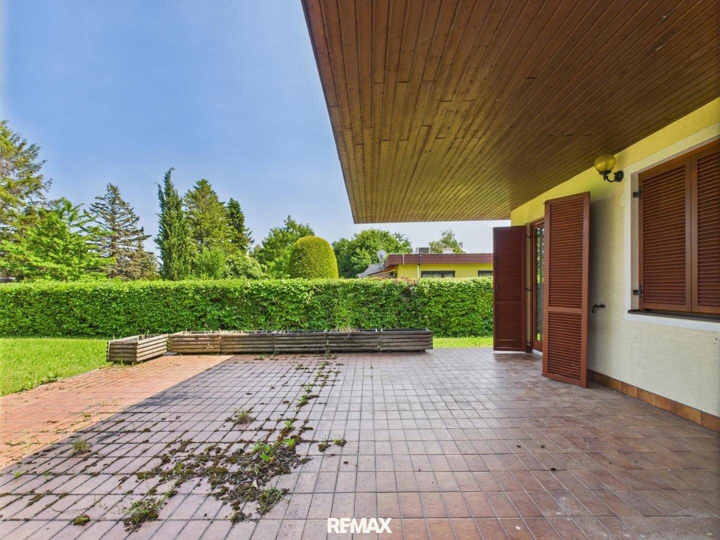 Geräumige Terrasse mit Fliesenboden, geöffneten Fensterläden und Zugang zum Garten.