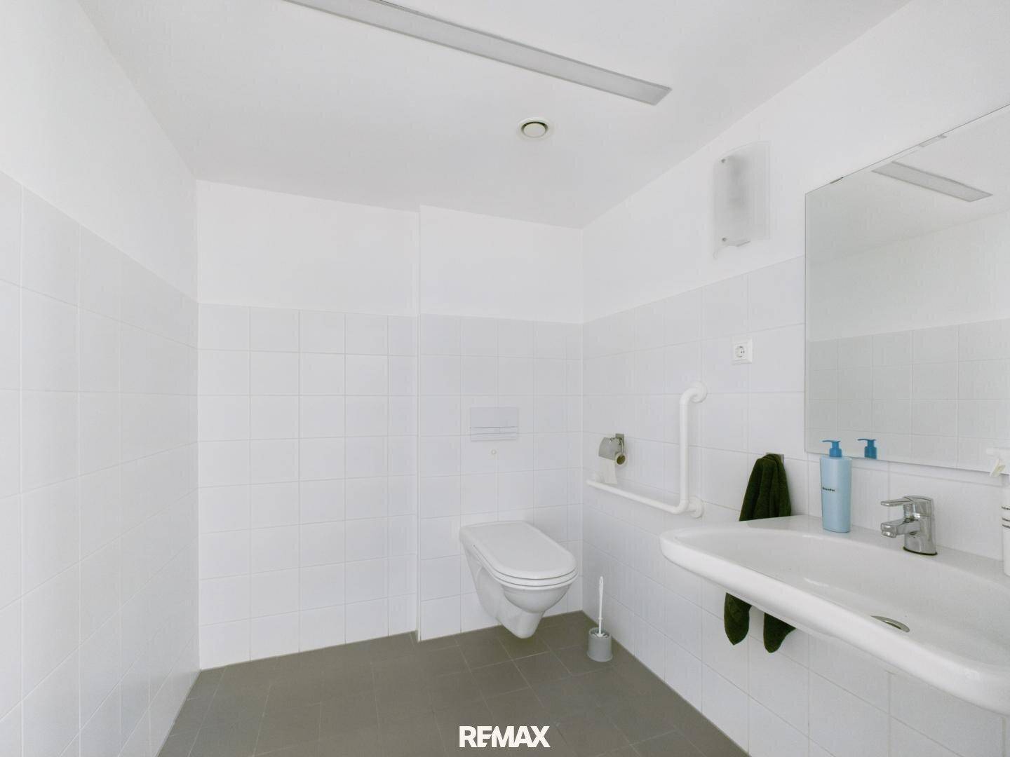 Barrierefreies Badezimmer mit Wand-WC, Waschbecken und Haltegriffen an den Wänden.
