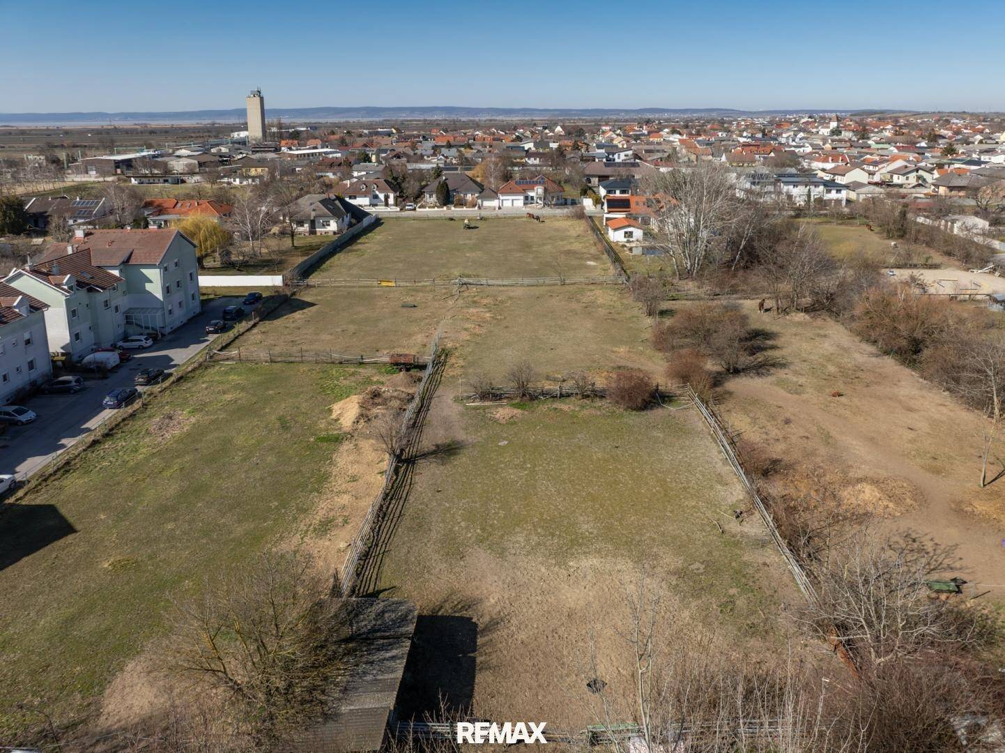Luftaufnahme des großen Grundstücks mit Weideflächen, angrenzenden Häusern und einem Wasserturm am Horizont.