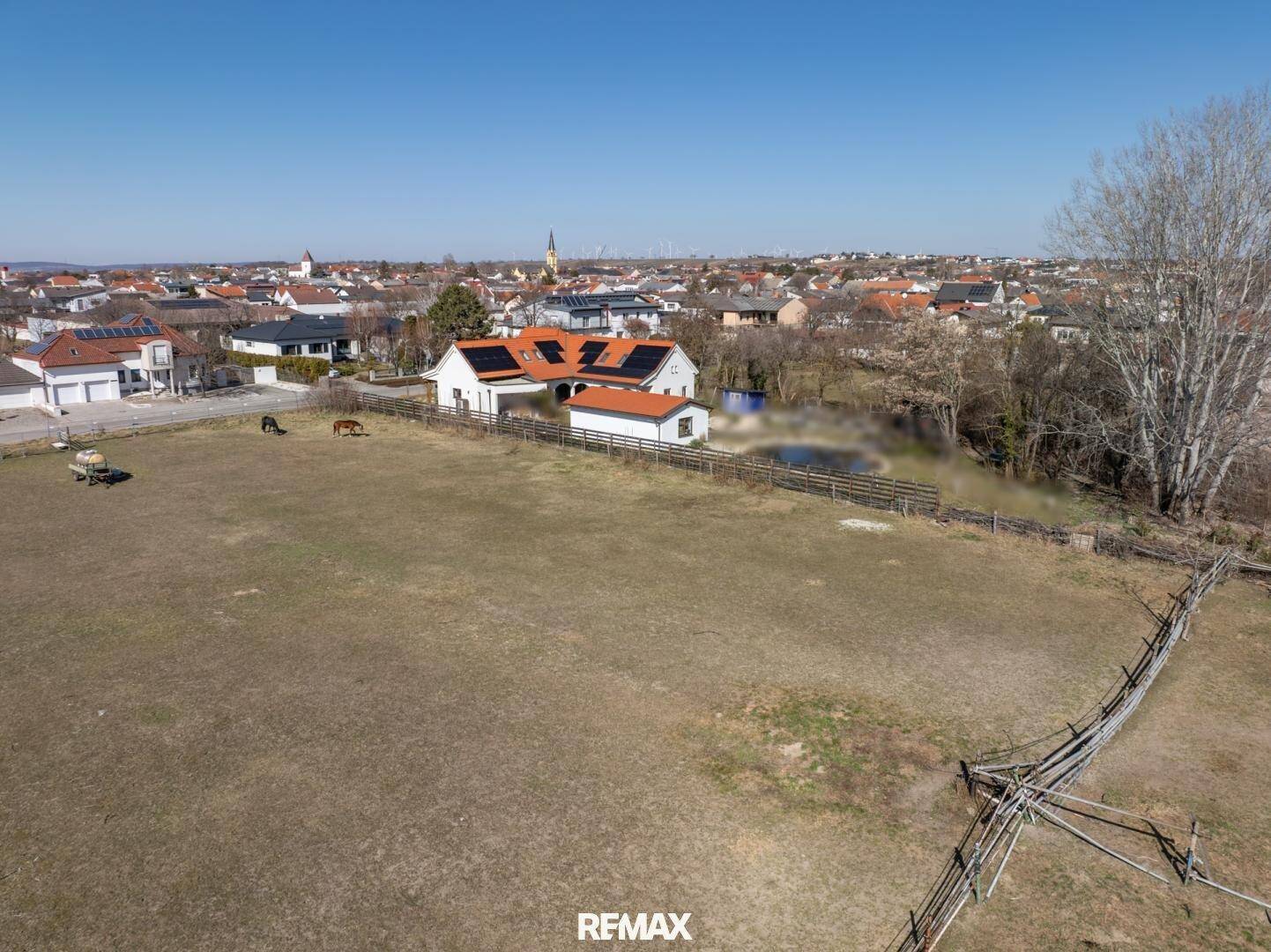 Luftaufnahme eines Wohnhauses mit Solaranlage und weitläufigem Weideland, umgeben von einer Siedlung.