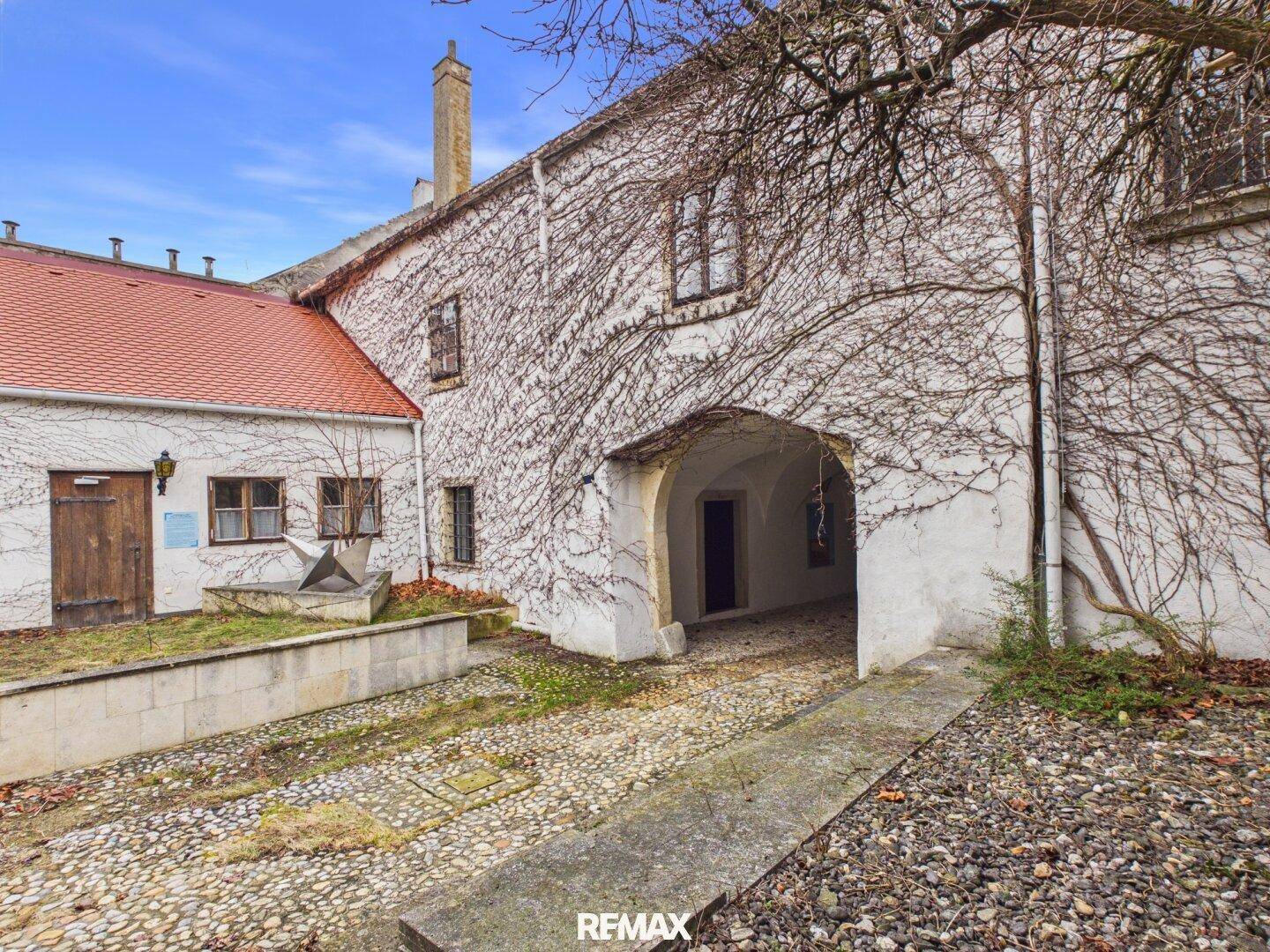 Historischer Innenhof mit Kieselsteinweg, von Efeu bewachsenen Mauern und einem Torbogen.