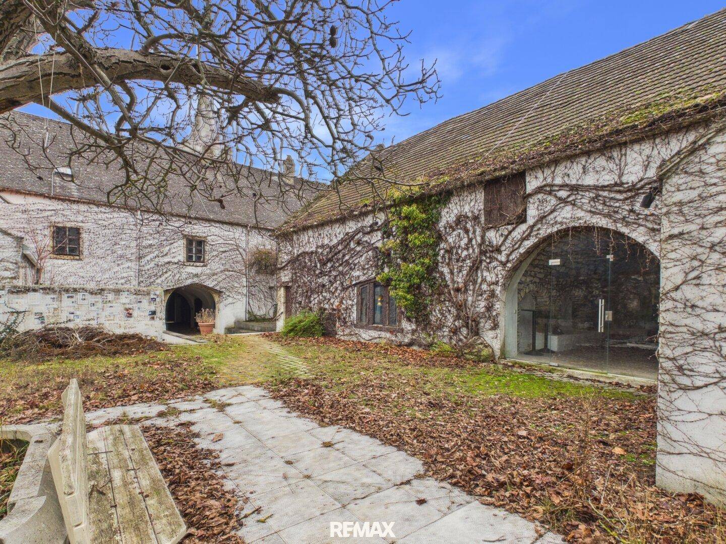Historischer Innenhof mit Steinplattenweg, bewachsenen Mauern und einem großen Torbogen.