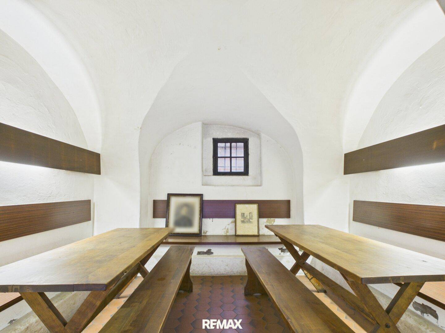 Rustikaler Speiseraum mit Holztischen und Bänken, Gewölbedecke und einem kleinen Fenster.