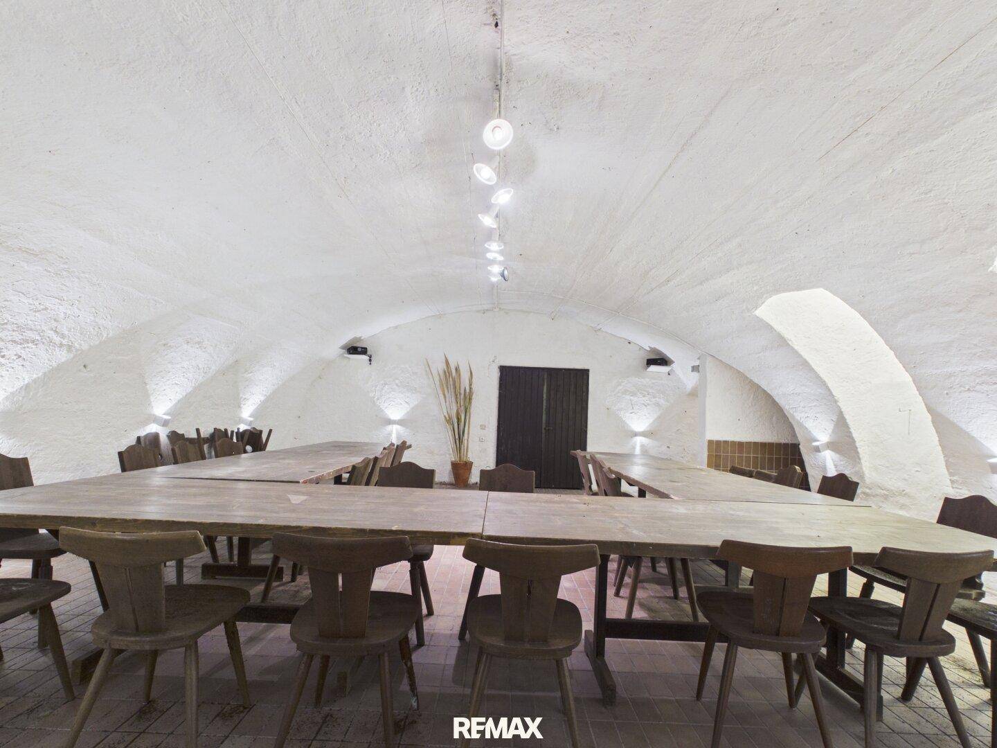 Großer Speisesaal mit langen Holztischen und Stühlen unter einer weißen Gewölbedecke.