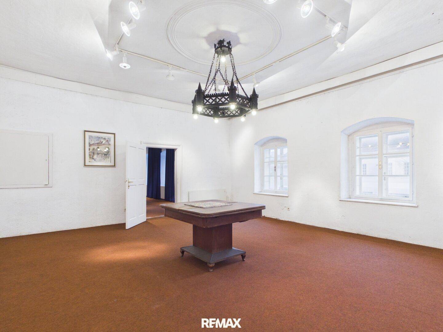 Großer Raum mit Stuckdecke, Kronleuchter und zwei Fenstern, ideal für festliche Anlässe.