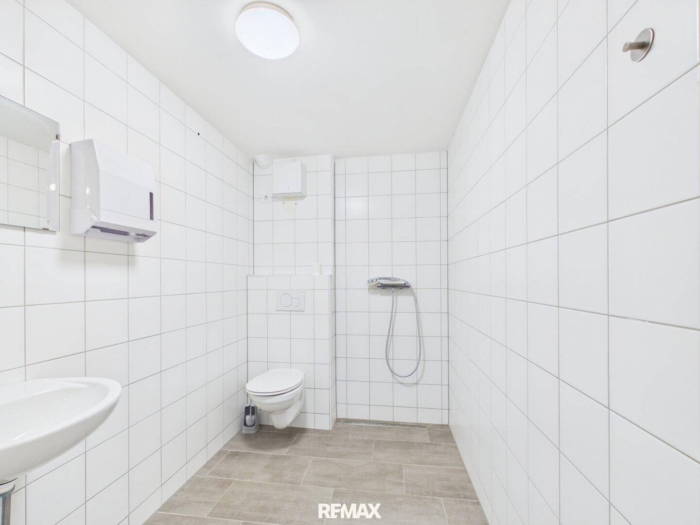 Helles Badezimmer mit weißen Fliesen, Dusche und WC, in einem sauberen und funktionalen Design.