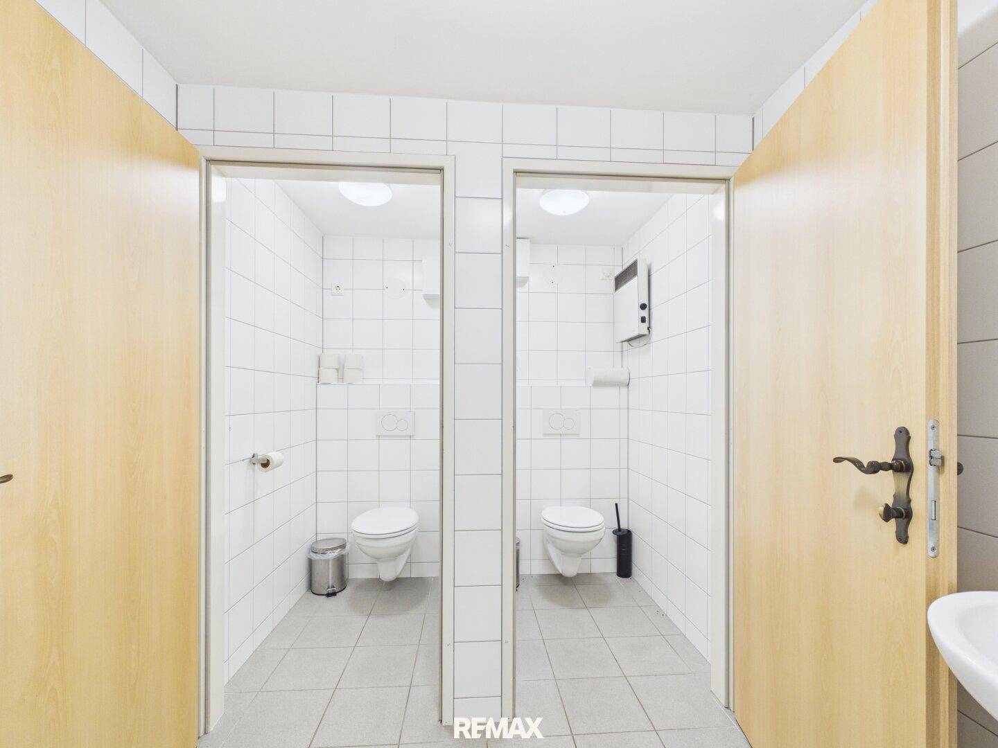 Zwei separate Toilettenkabinen mit weißen Fliesen und modernen WCs, sauber und funktional.