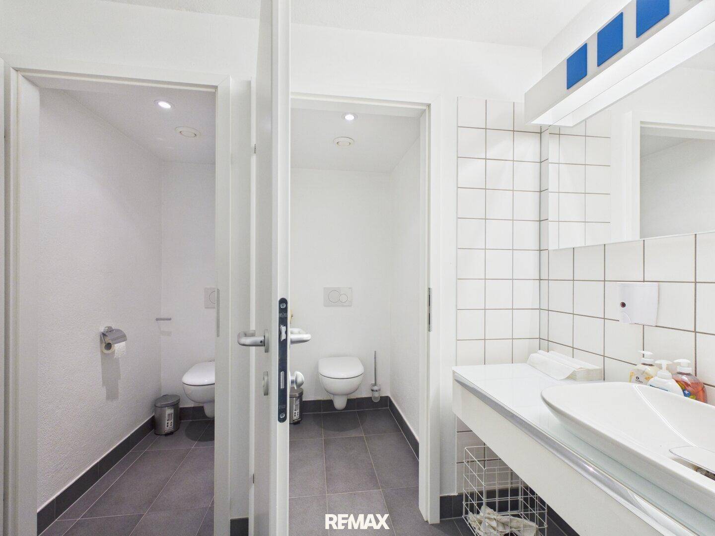 Mehrere Toilettenkabinen mit Waschbecken und Spiegel in einem modernen Sanitärbereich.