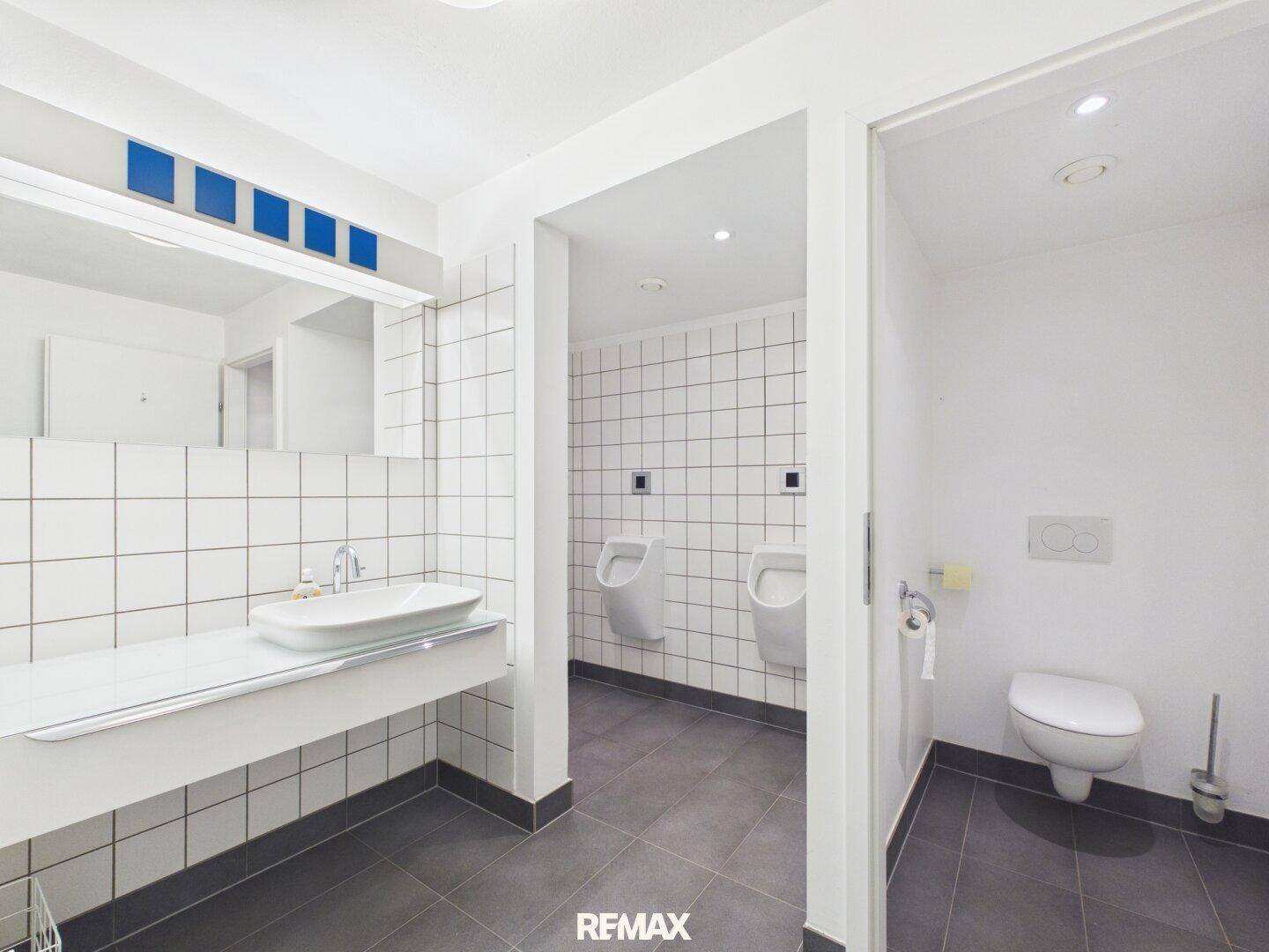 Moderner Sanitärbereich mit Waschbecken, Urinalen und Toilettenkabinen, hell und funktional gestaltet.