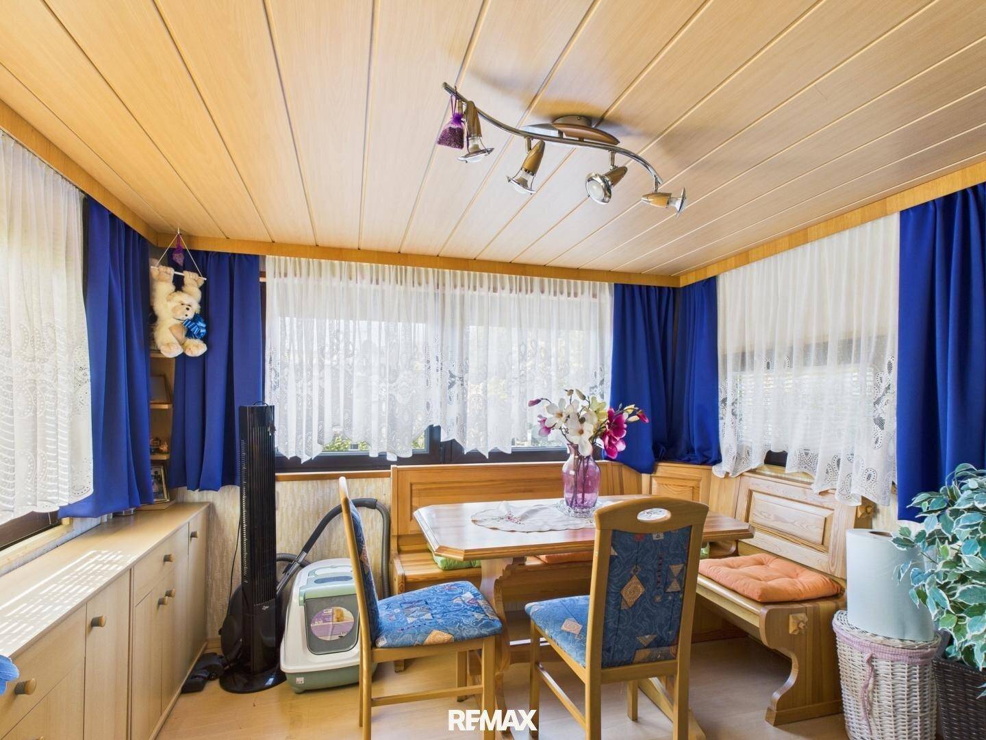 Gemütlicher Essbereich mit Holztäfelung an Decke und Wänden, blauen Vorhängen und rustikaler Sitzbank.