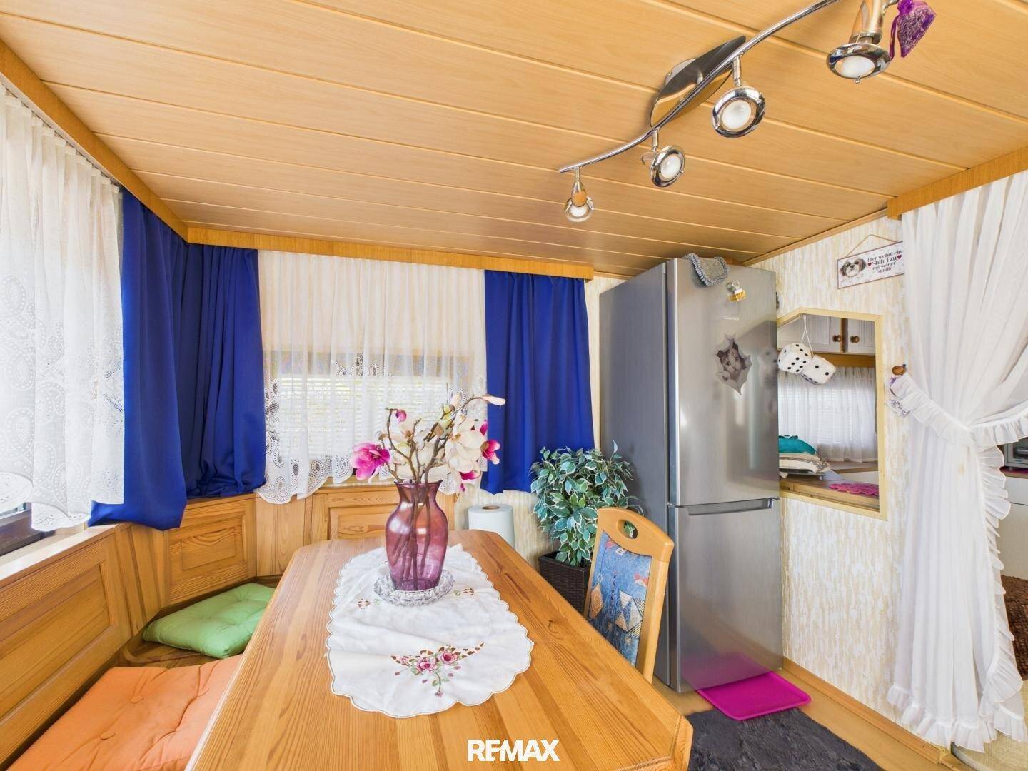 Essbereich mit Holztisch, Sitzbank und einem Kühlschrank, der praktisch in den Raum integriert ist.