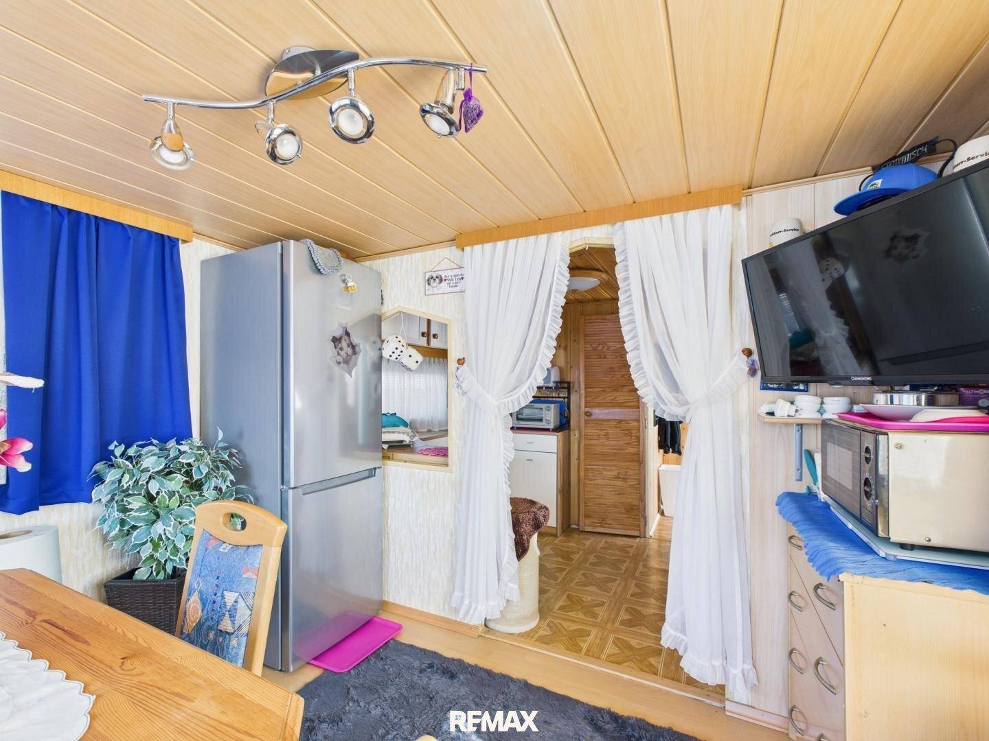 Essbereich mit Kühlschrank und Blick auf einen angrenzenden Raum, ausgestattet mit einem Fernseher.