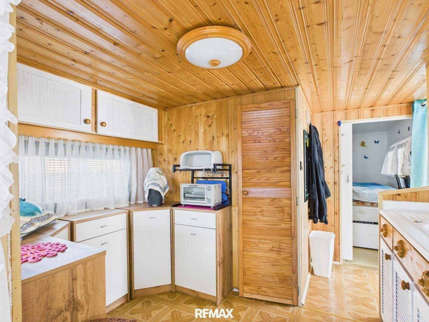 Kleine Küchenzeile mit weißen Schränken, Holztäfelung und Blick in ein angrenzendes Schlafzimmer.