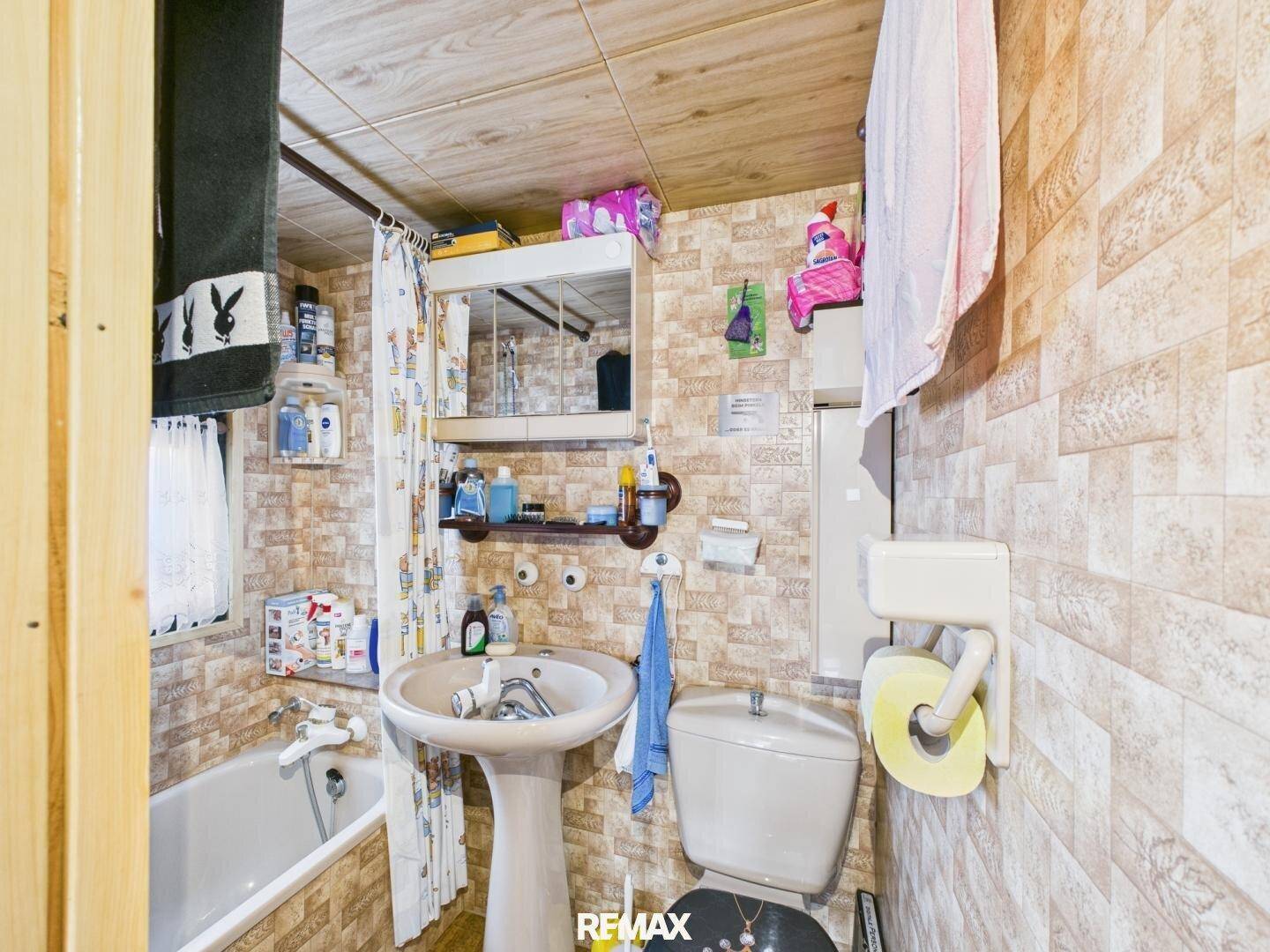 Kleines Badezimmer mit Waschbecken, Toilette und Badewanne, umgeben von gemusterten Fliesen.