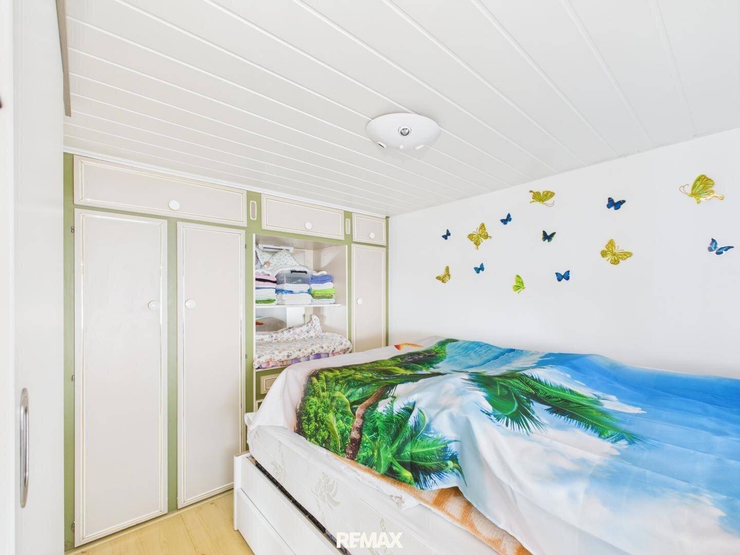 Gemütliches Schlafzimmer mit Bett, Einbauschränken und verspielten Schmetterlings-Wandstickern für Kinder.