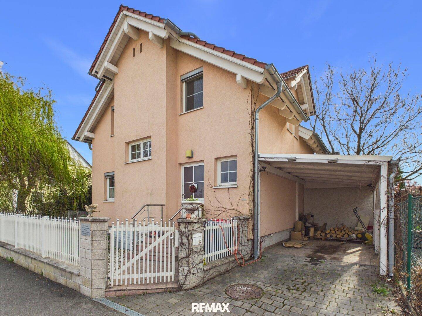 Seitenansicht des Hauses mit rosa Fassade, Carport und gepflasterter Einfahrt.