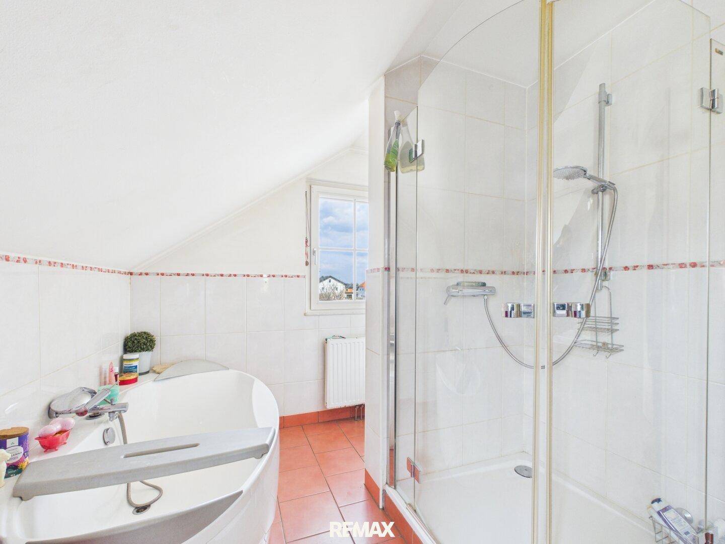 Helles Badezimmer im Dachgeschoss mit Dusche, Badewanne und Fenster.