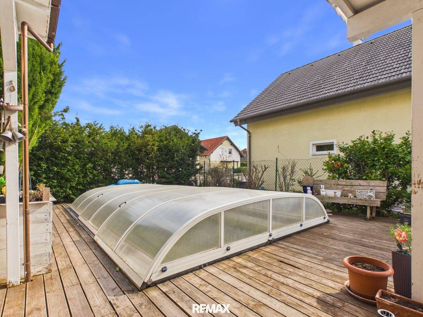 Gartenbereich mit großem Holzdeck und einem abgedeckten Swimmingpool unter blauem Himmel.
