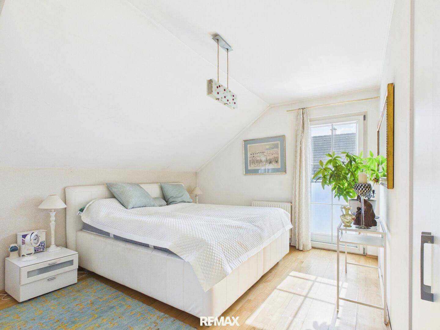 Gemütliches Schlafzimmer im Dachgeschoss mit Doppelbett, Holzboden und Zugang zum Balkon.