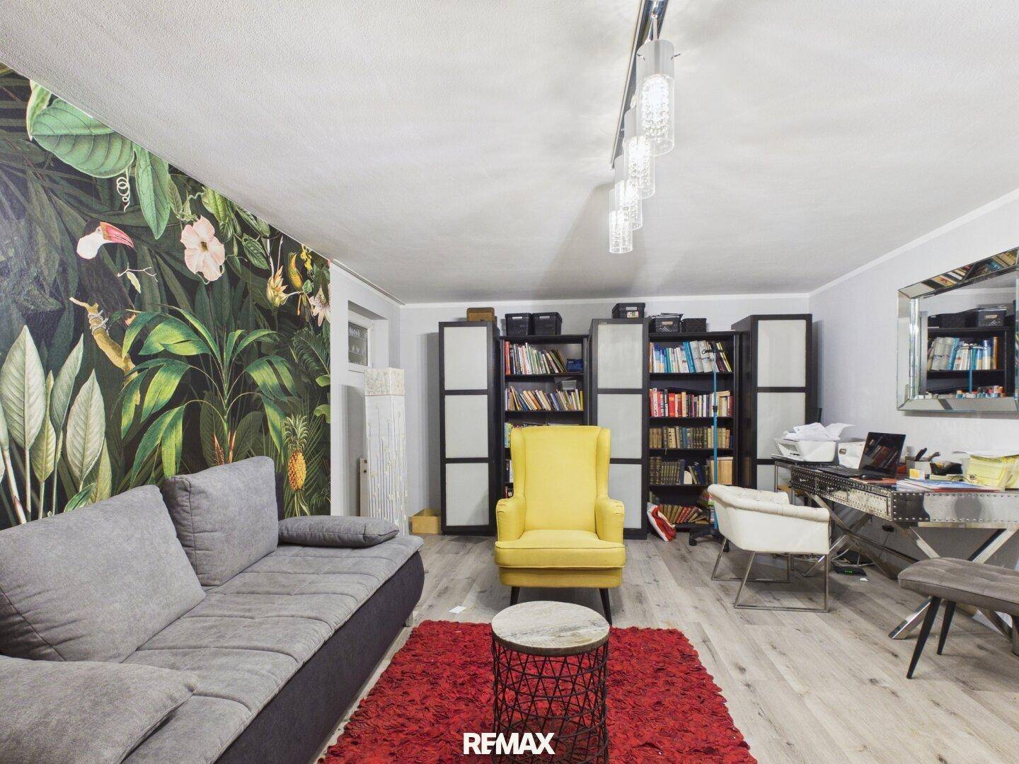 Modern eingerichtetes Wohnzimmer mit farbenfroher Tapete, Bücherregalen und Schreibtischbereich.