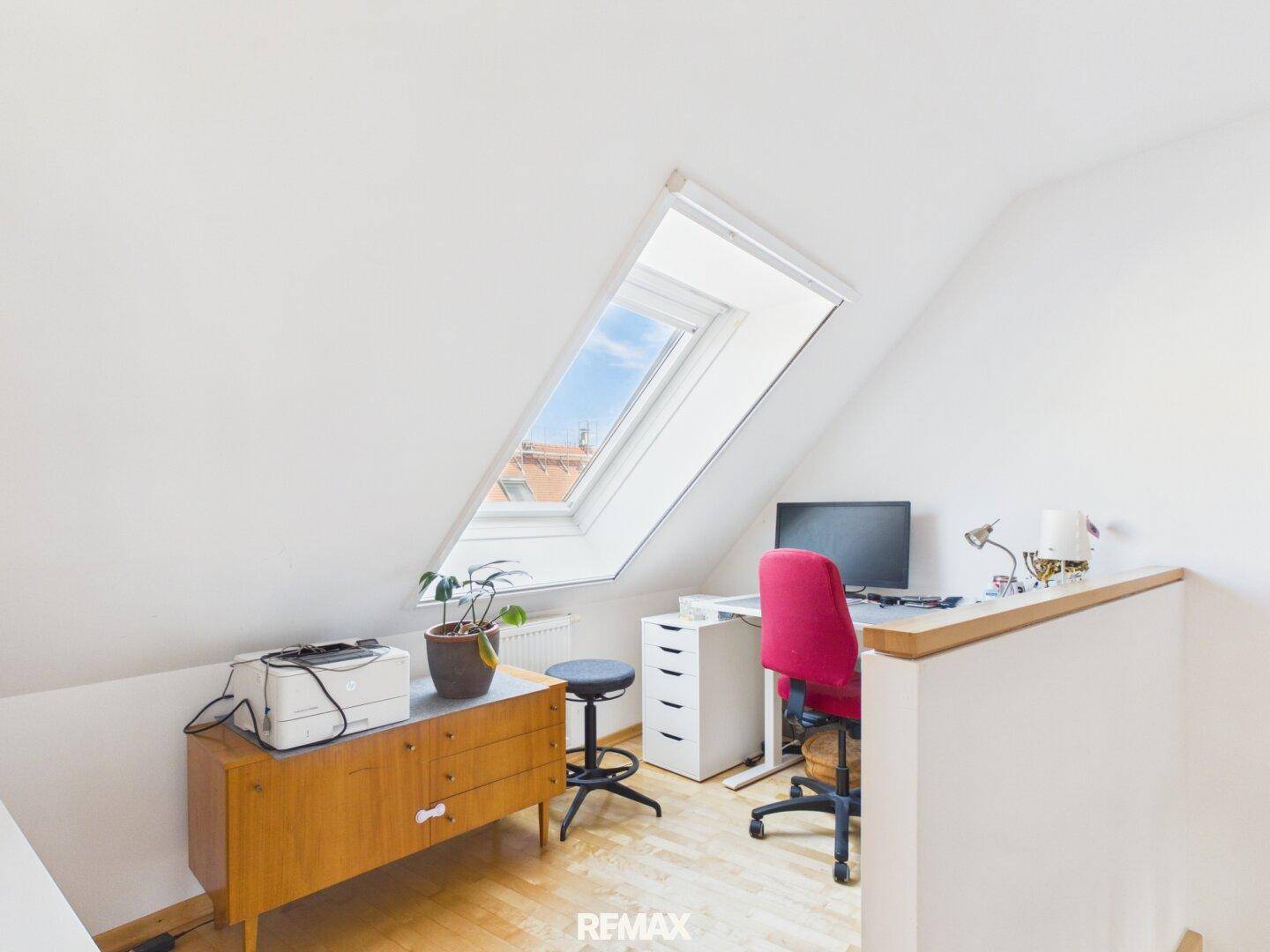 Ruhiges Arbeitszimmer im Dachgeschoss mit Schreibtisch, Computer und viel Tageslicht durch das Dachfenster.