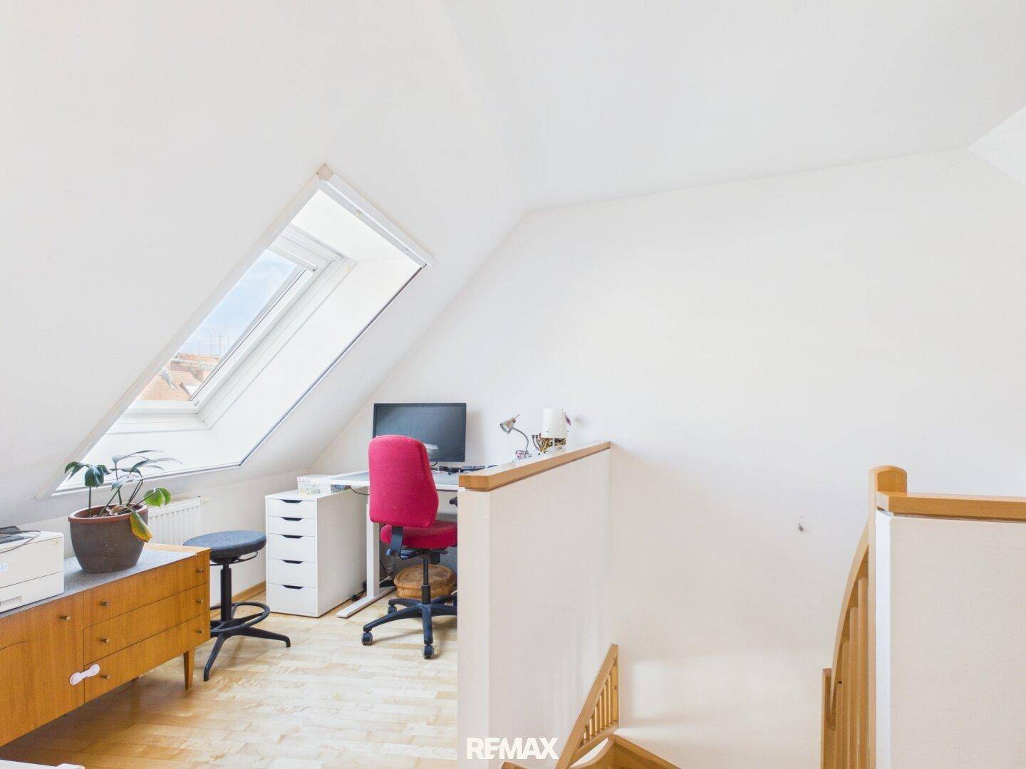 Heller Arbeitsbereich mit Dachschräge, Schreibtisch und Blick ins Freie durch das Dachfenster.