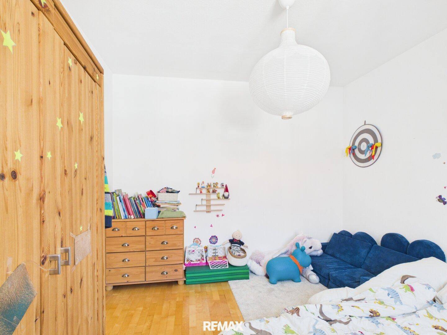 Helles Kinderzimmer mit Holzschrank, Kommode und spielerischen Elementen unter der Dachschräge.