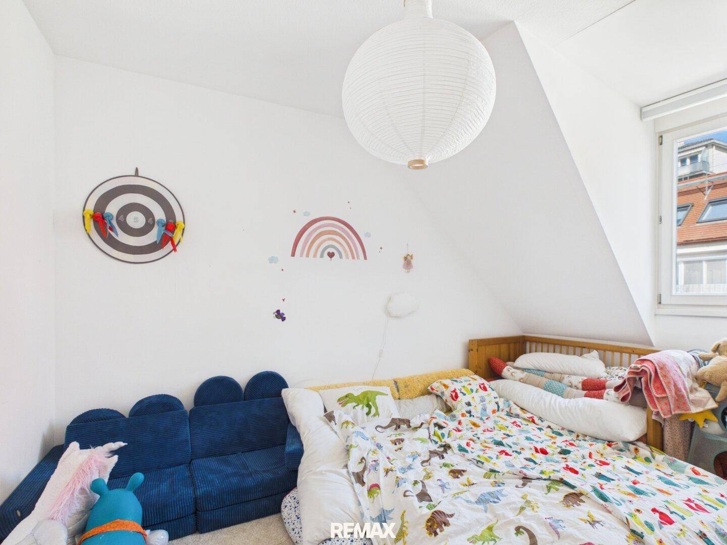 Kinderzimmer mit Bett, blauer Sitzgelegenheit und verspielten Wanddekorationen unter der Dachschräge.