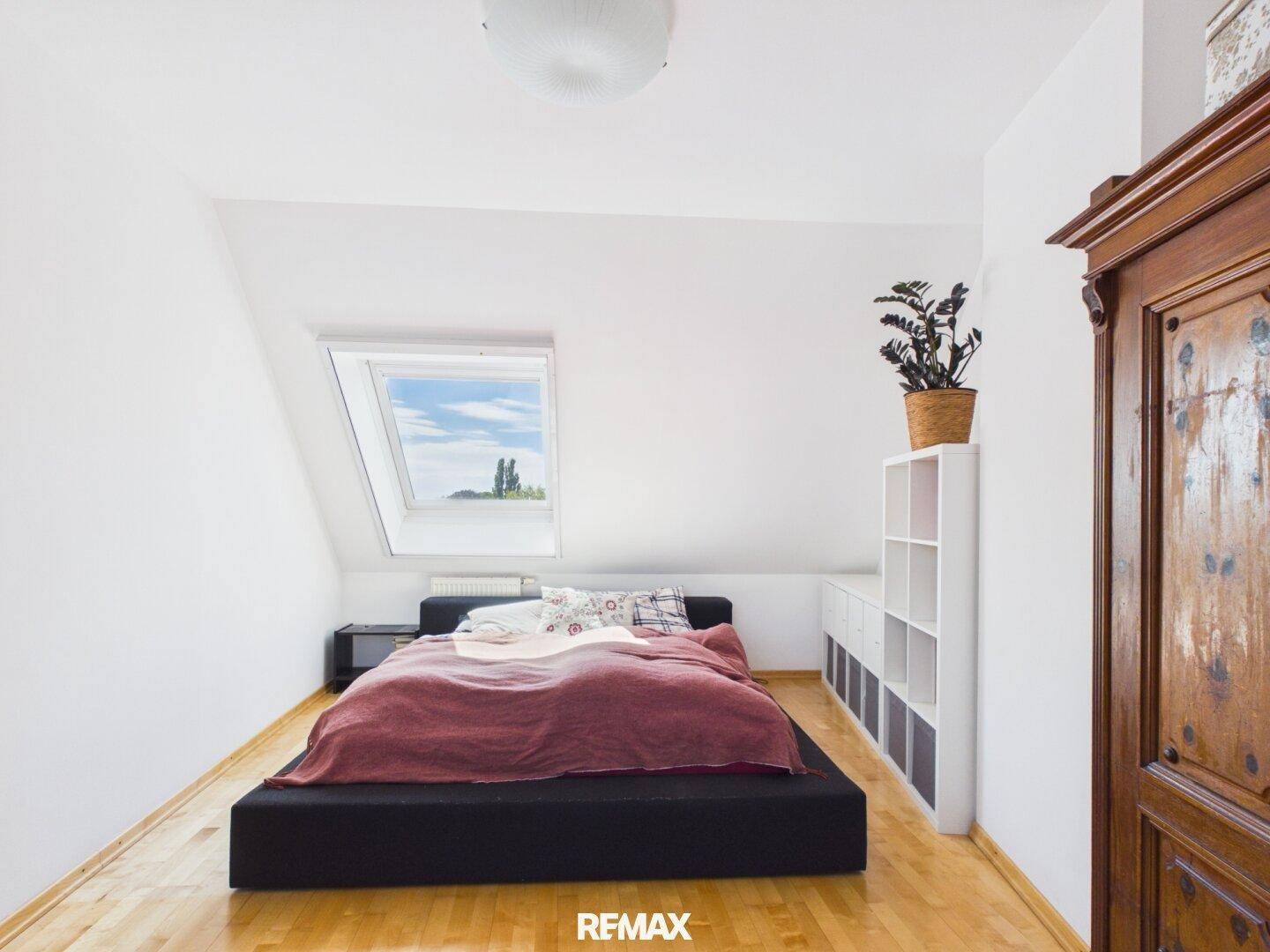 Schlafzimmer im Dachgeschoss mit Bett, Regal und hellem Dachfenster für natürliche Belichtung.