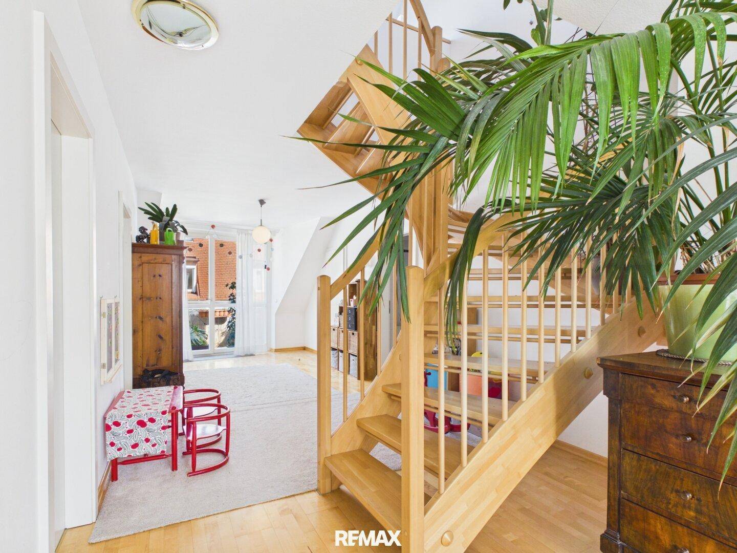 Heller Flur mit Holztreppe, Pflanzen und Zugang zu einem Außenbereich.