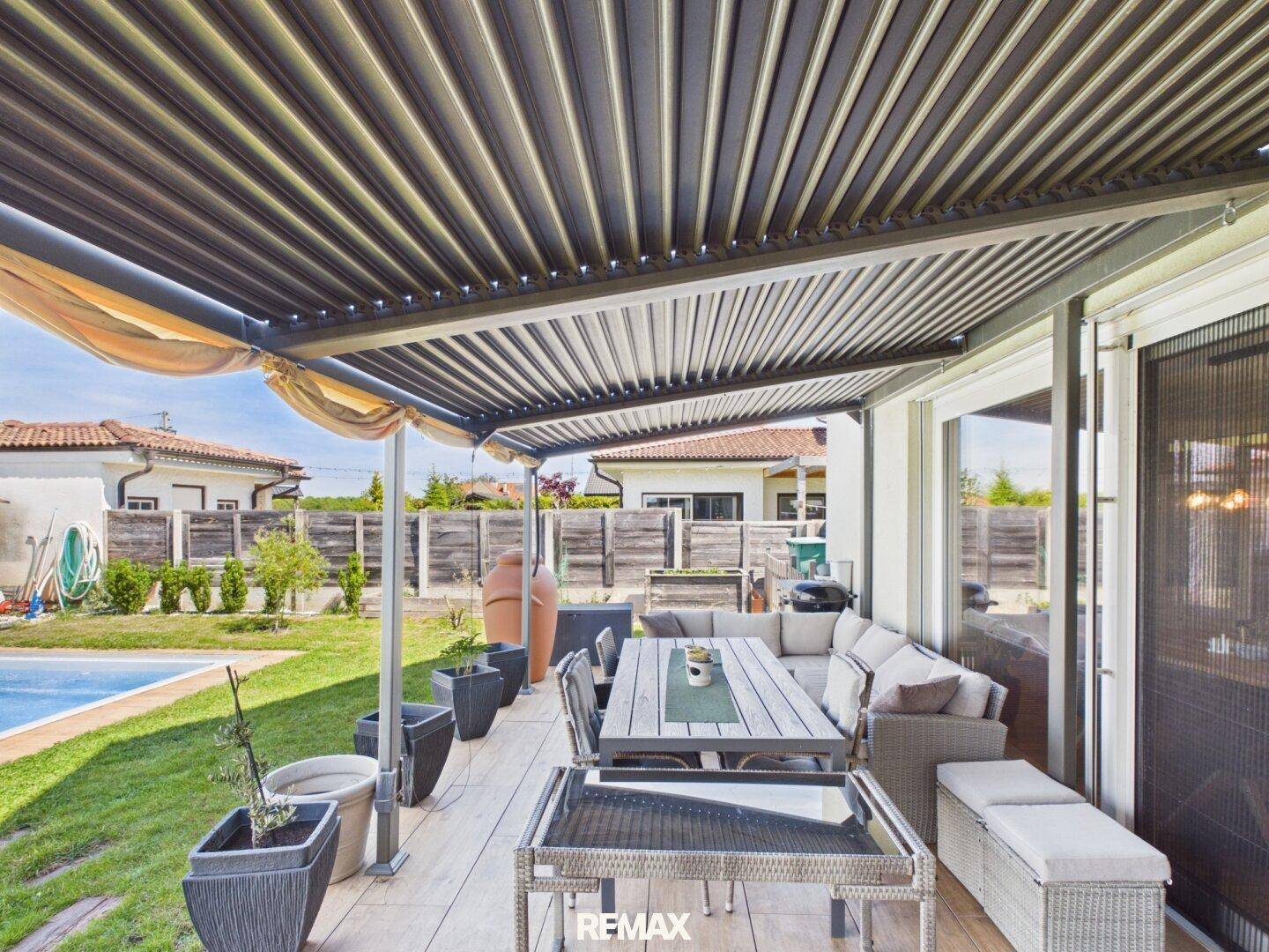 Überdachte Terrasse mit modernen Gartenmöbeln und Blick auf den Poolbereich im Garten.