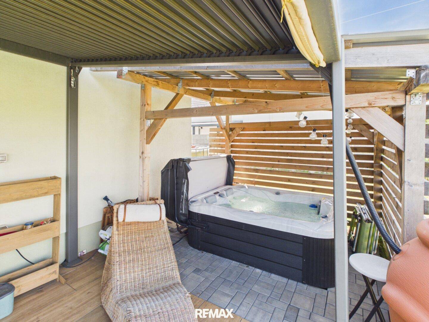 Entspannungsbereich auf der Terrasse mit einem Whirlpool unter einer schützenden Holzkonstruktion.