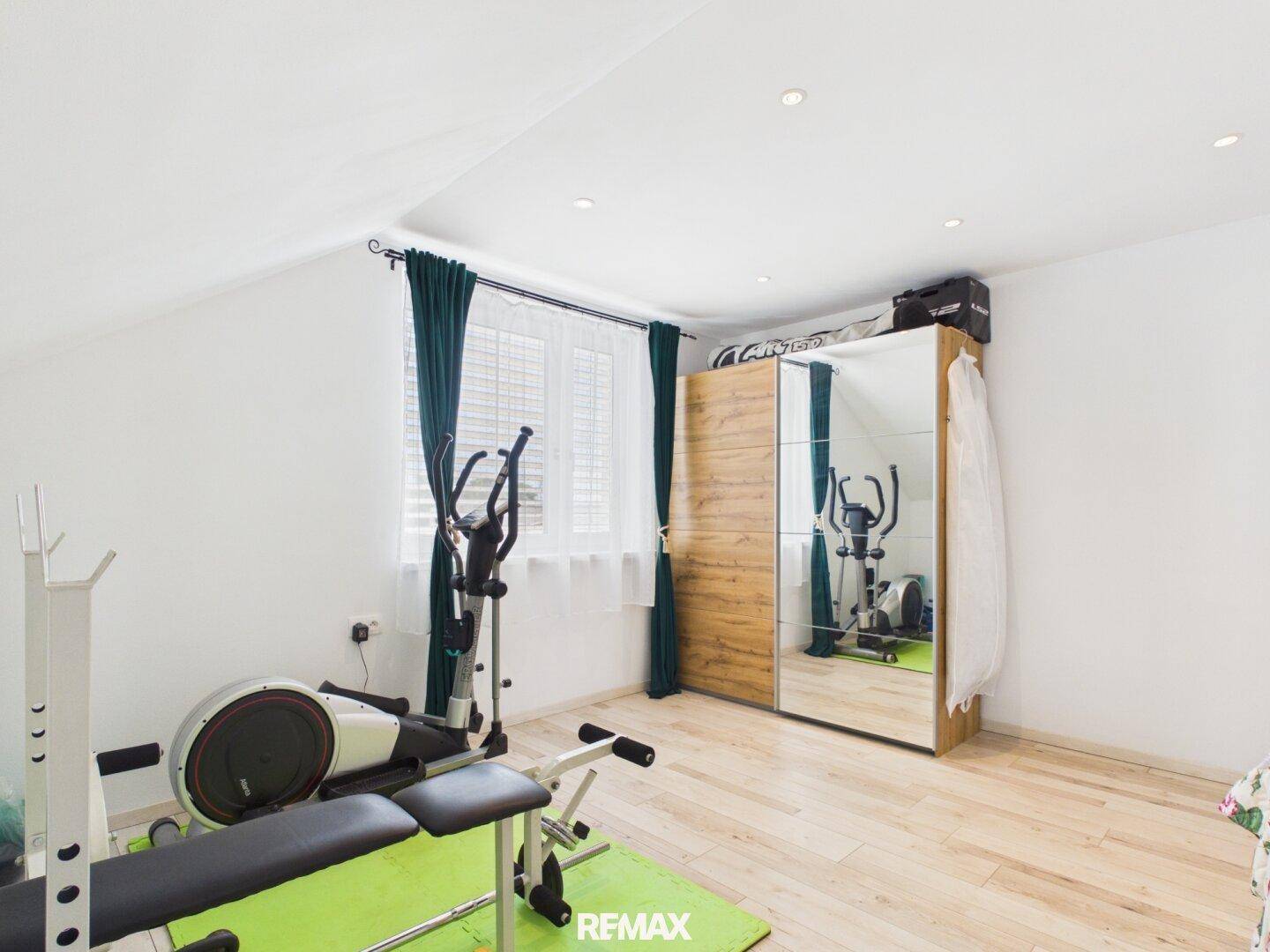 Helles Schlafzimmer im Dachgeschoss mit Fitnessgeräten und großem Spiegelschrank.