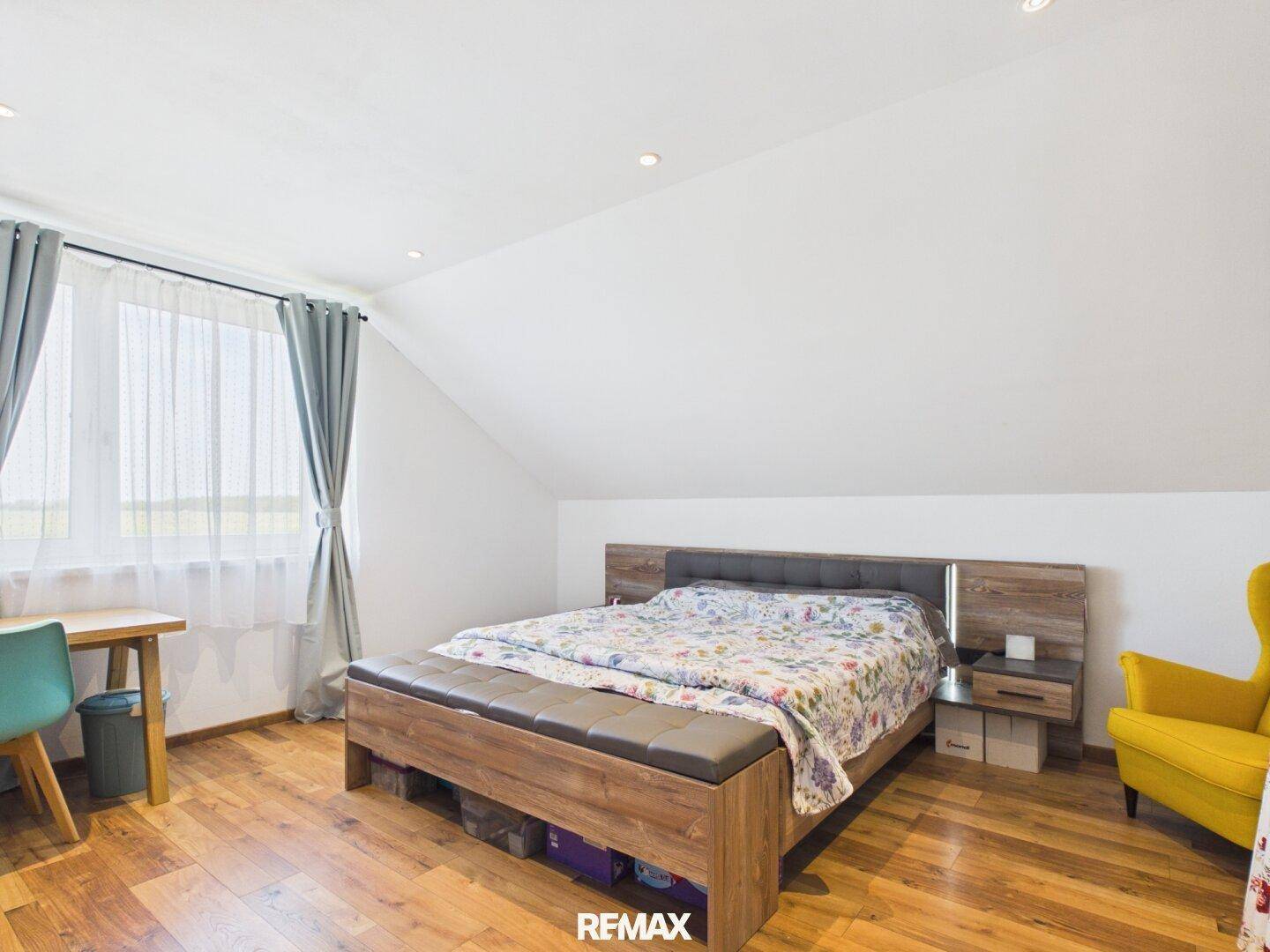 Gemütliches Schlafzimmer im Dachgeschoss mit Holzboden, Doppelbett und gelbem Sessel.