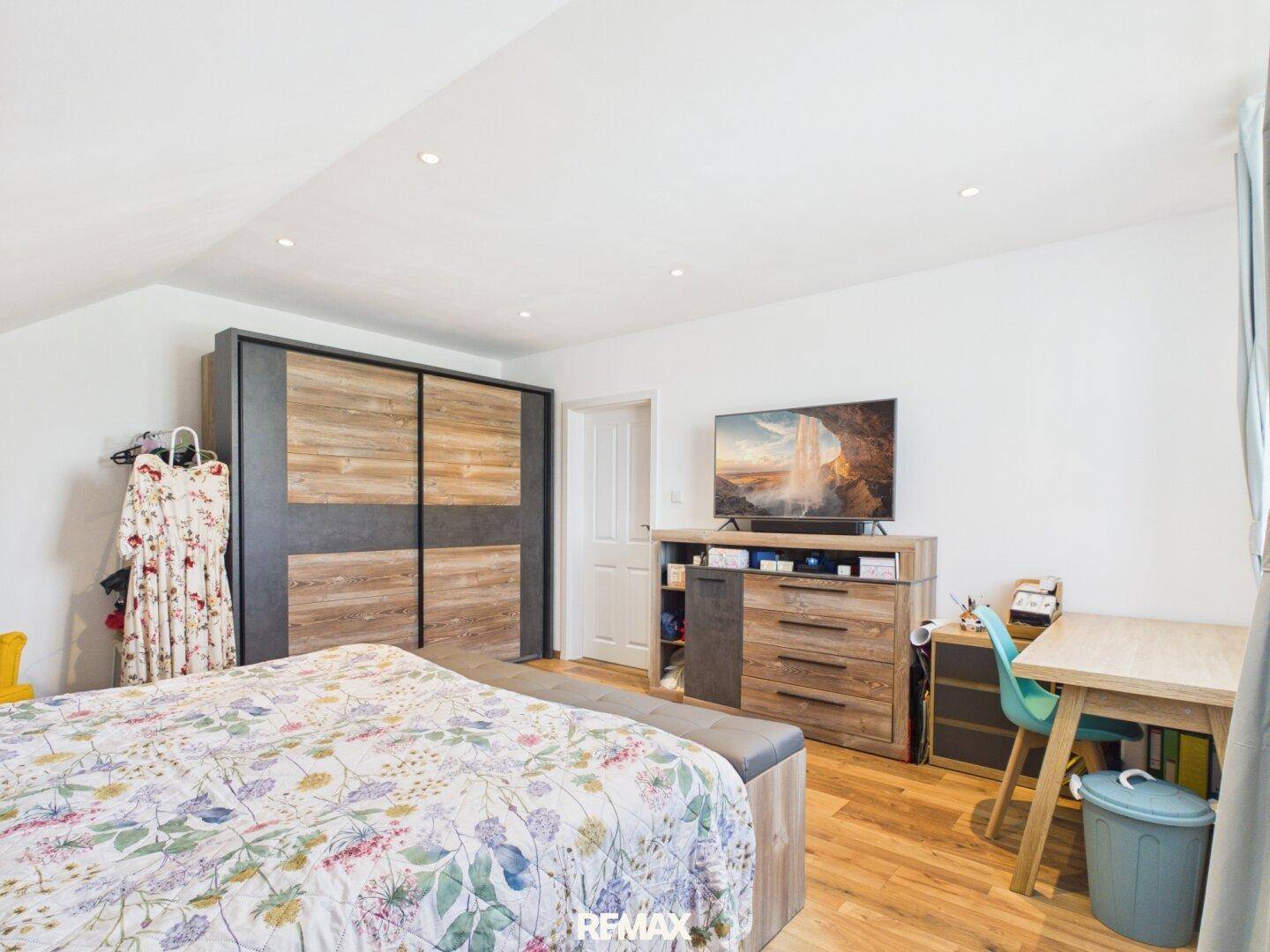 Helles Schlafzimmer im Dachgeschoss mit Holzboden, großem Bett und modernem Kleiderschrank.