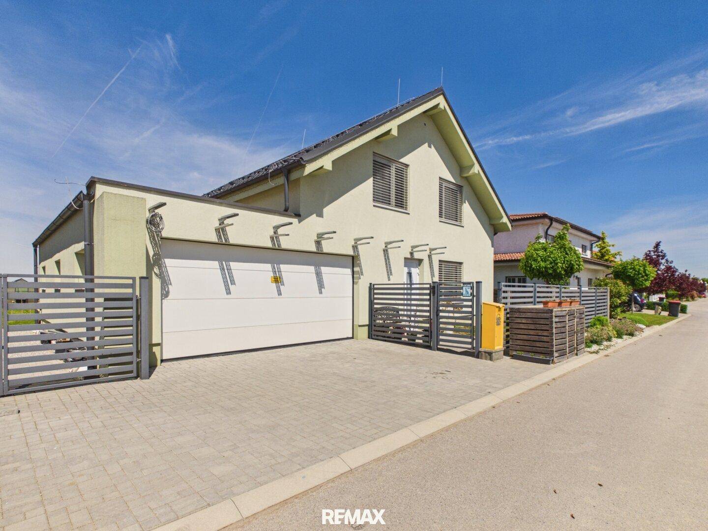 Modernes Einfamilienhaus mit integrierter Garage, gepflasterter Auffahrt und Zaun.