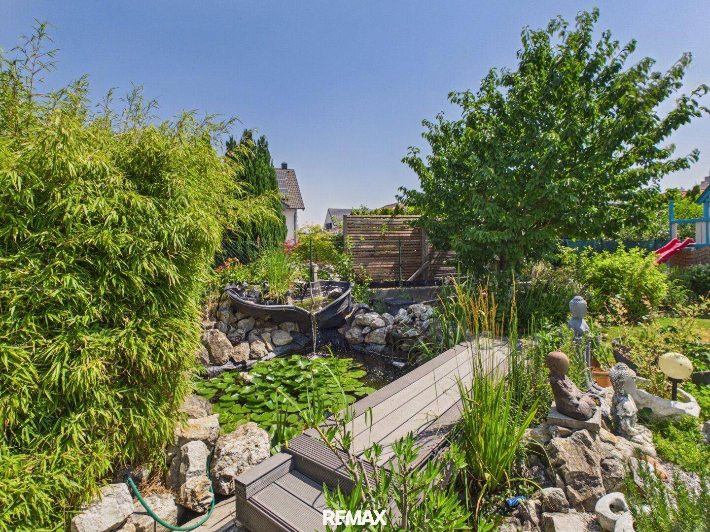 Naturnaher Garten mit Teich, Holzsteg und üppiger Bepflanzung.