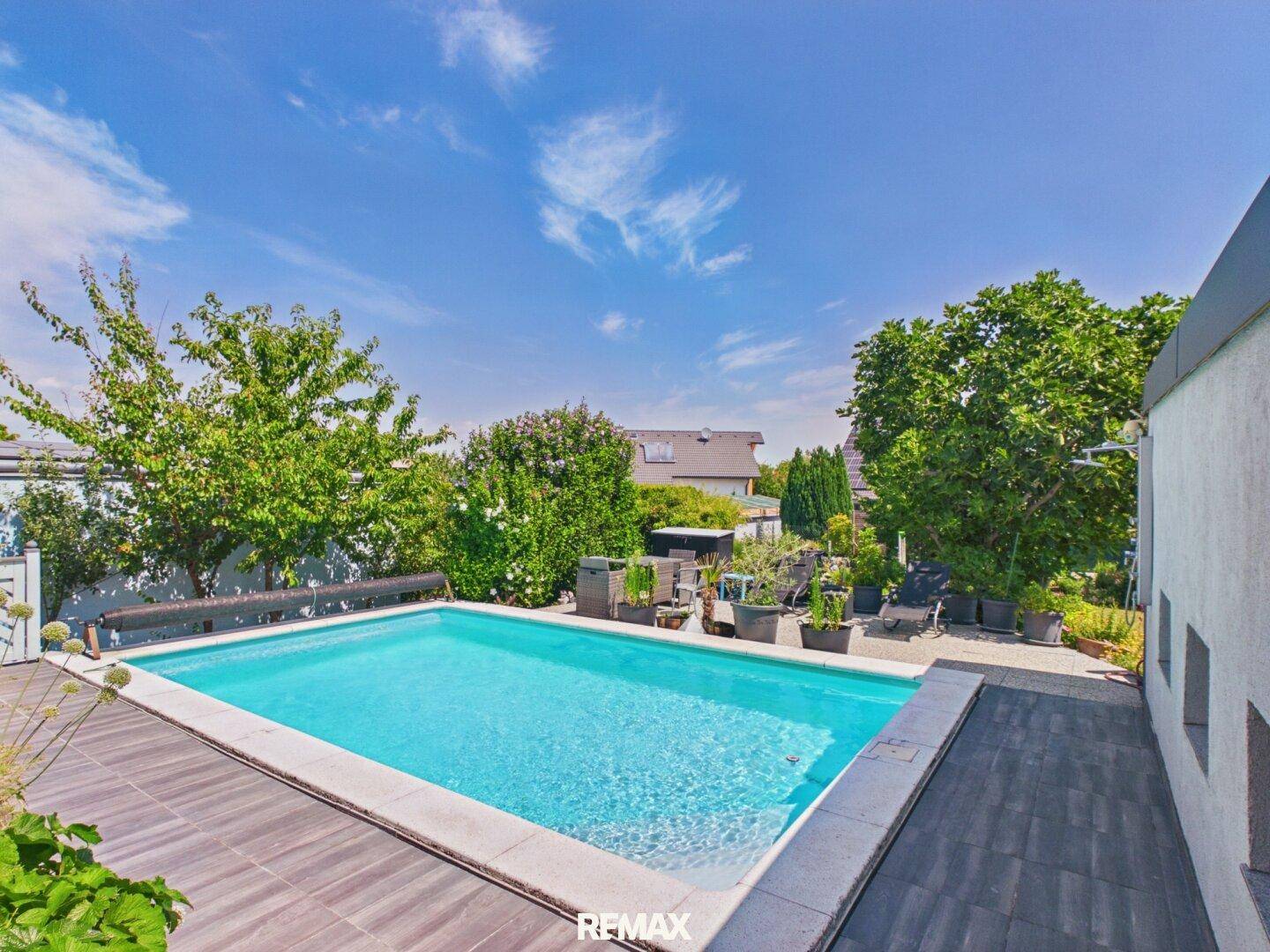 Großer Swimmingpool im Garten mit Holzdeck und viel Grünfläche um das Poolhaus.