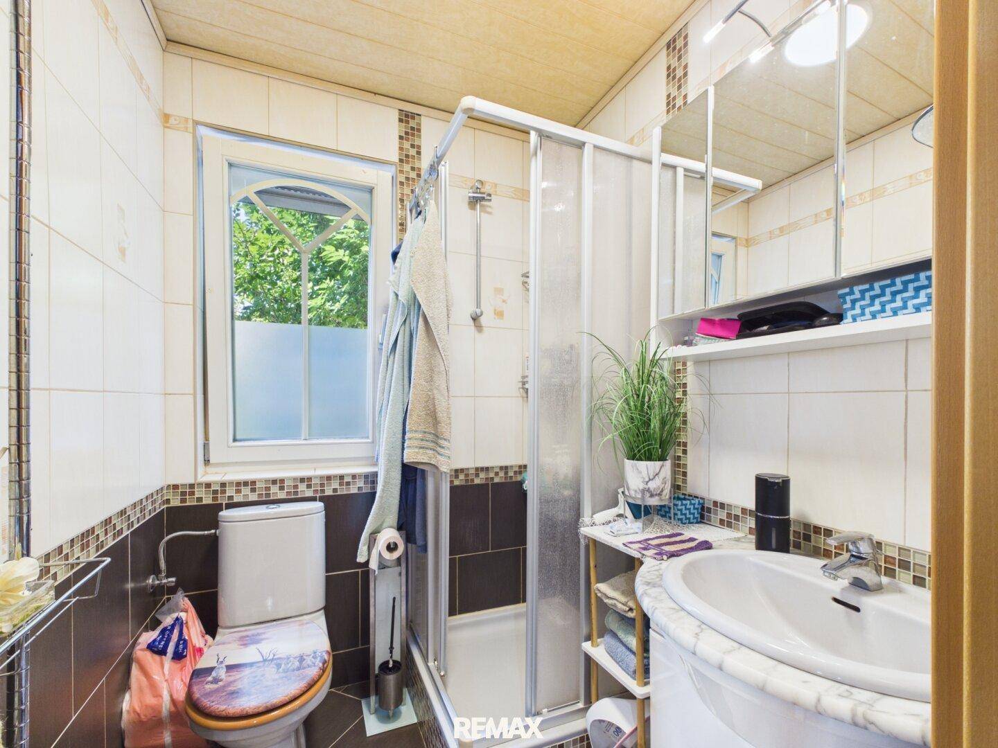 Kleines Badezimmer mit Dusche, WC und Fenster.