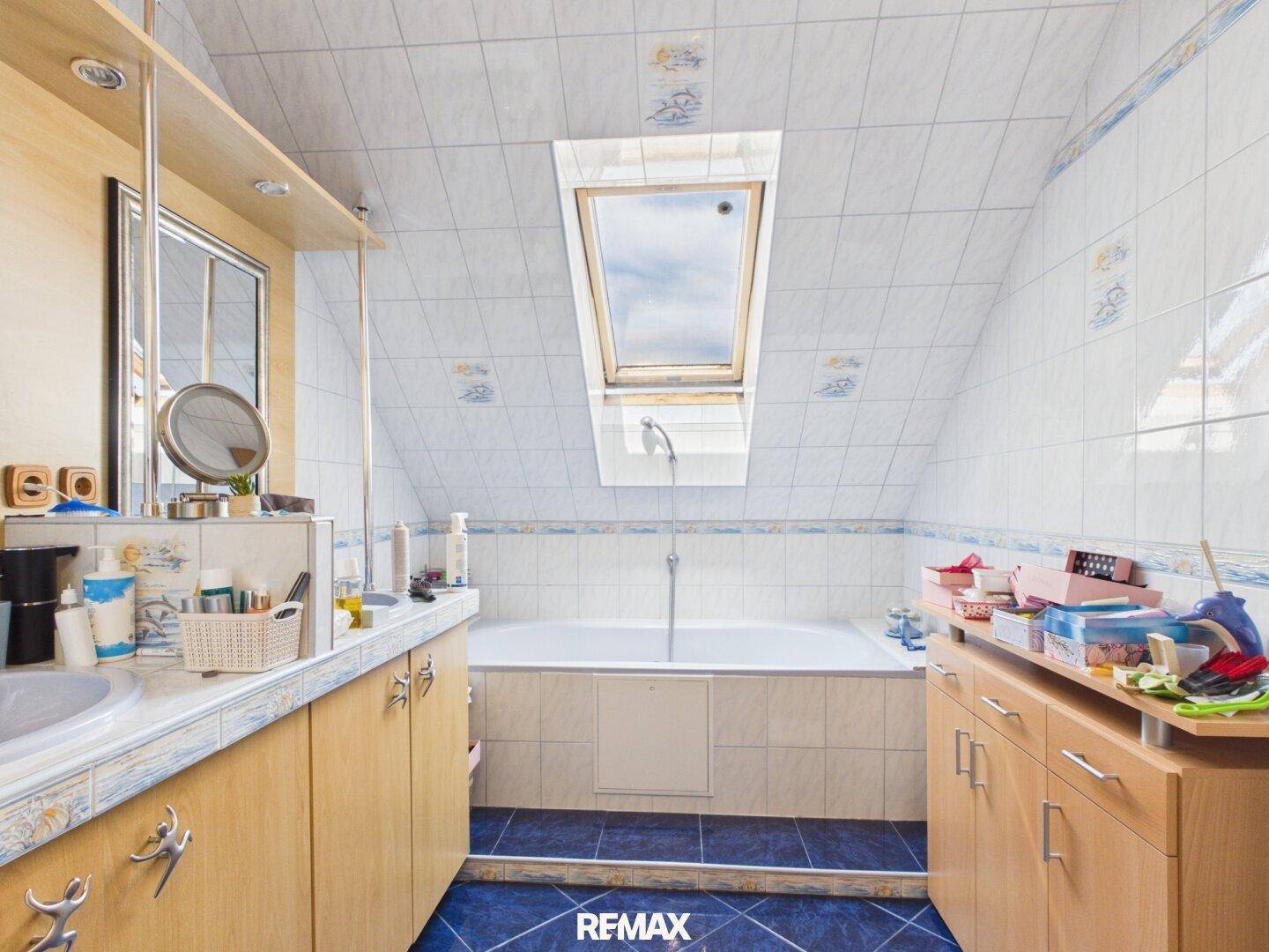 Geräumiges Badezimmer im Dachgeschoss mit Badewanne, Dachfenster und Fliesen.