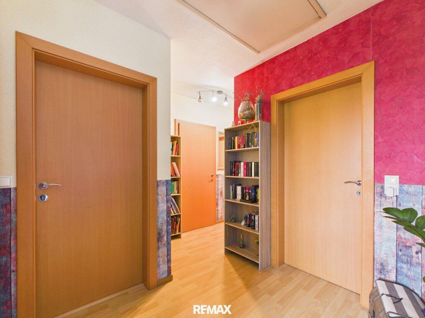 Flur mit Holzboden, Bücherregal und farbigen Wänden.