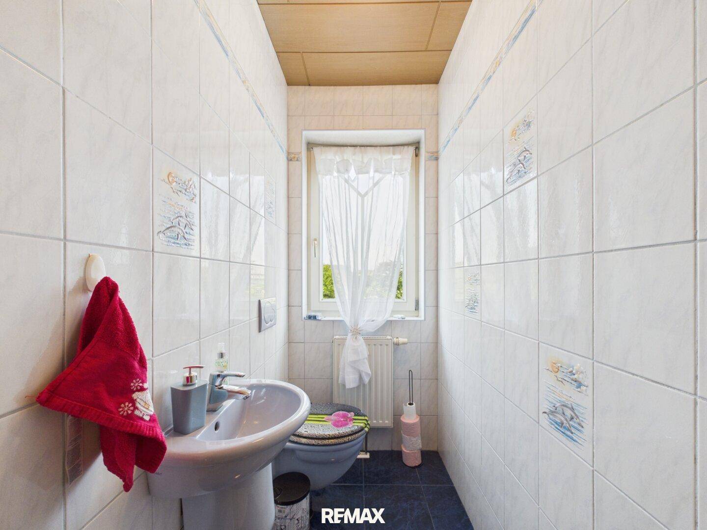 Separates WC mit Fenster, Waschbecken und Fliesen an den Wänden.