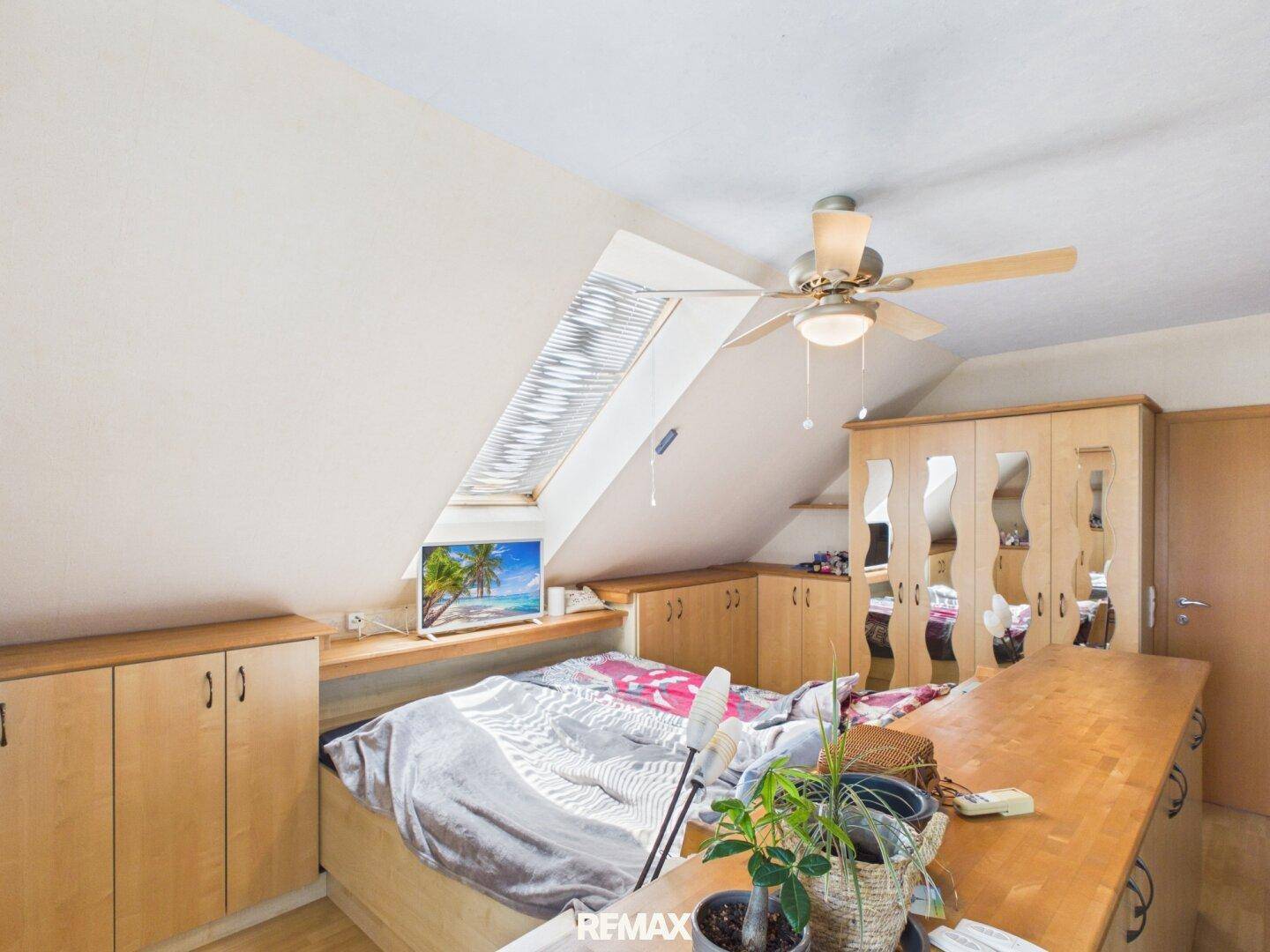 Gemütliches Schlafzimmer im Dachgeschoss mit Dachfenster, Deckenventilator und Einbauschränken.