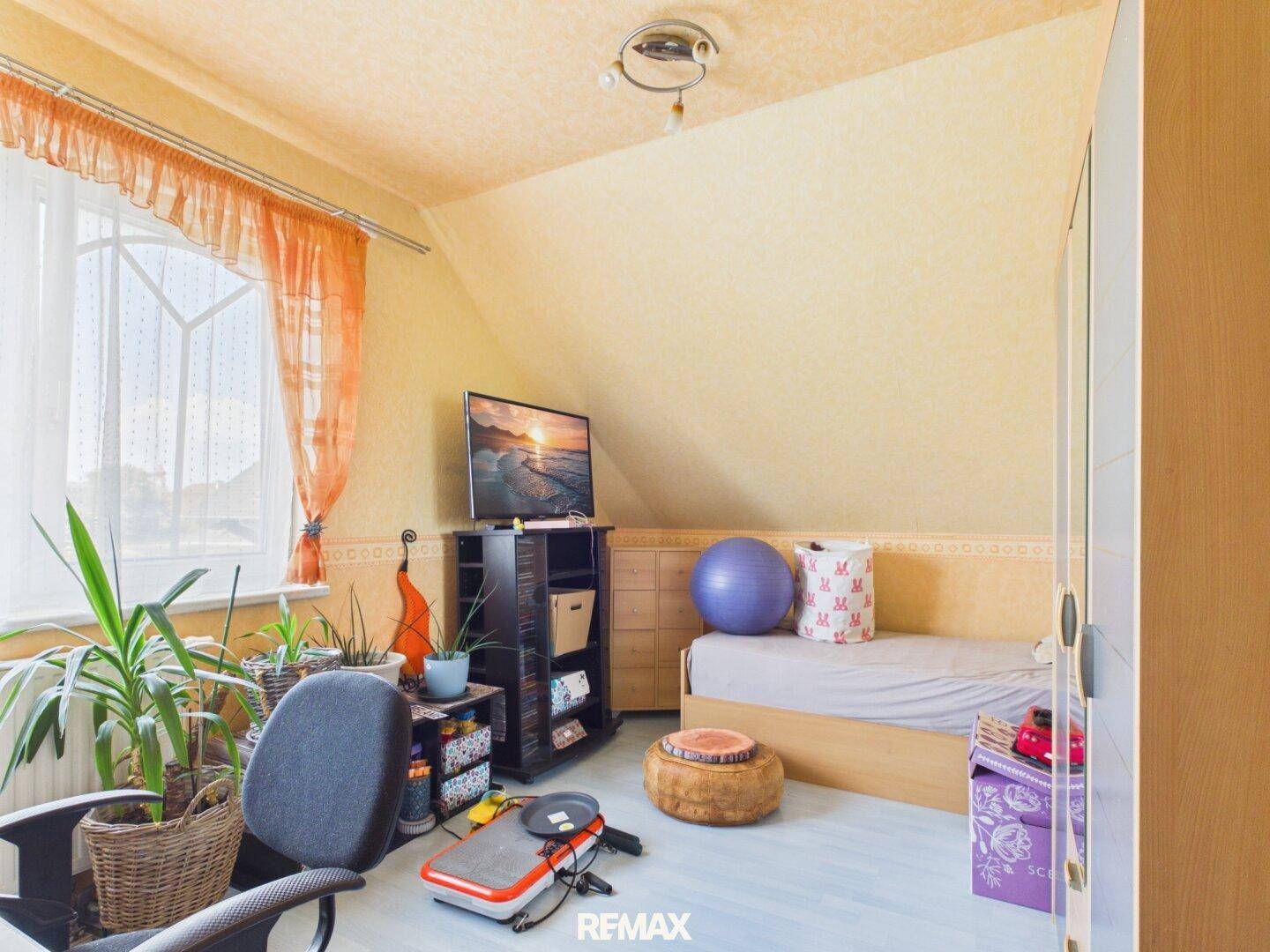 Helles Kinder- oder Gästezimmer im Dachgeschoss mit Fenster, Bett und Schreibtischbereich.
