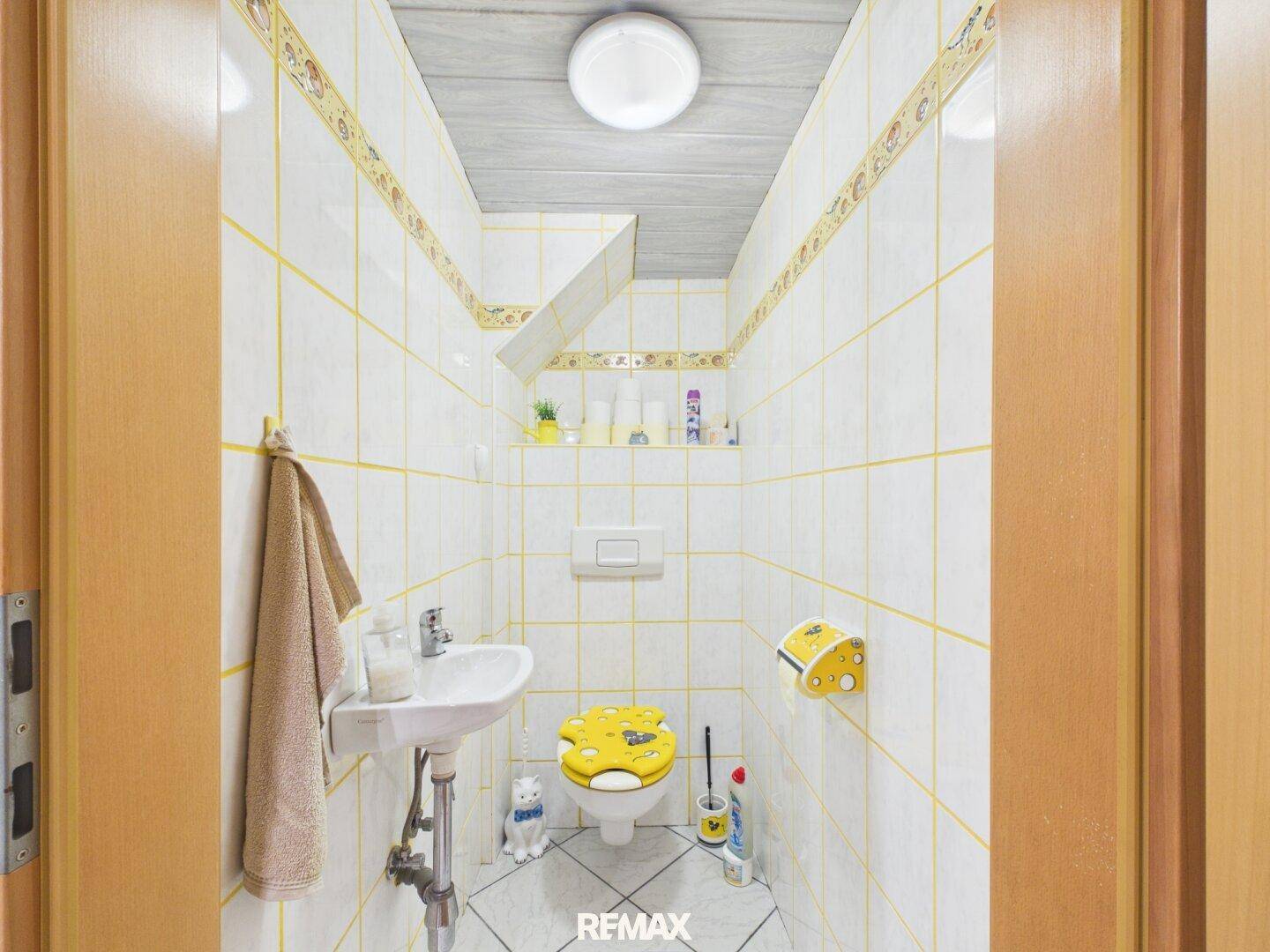 Kleines Gäste-WC mit gelben Fliesen, Waschbecken und verspielter Dekoration.