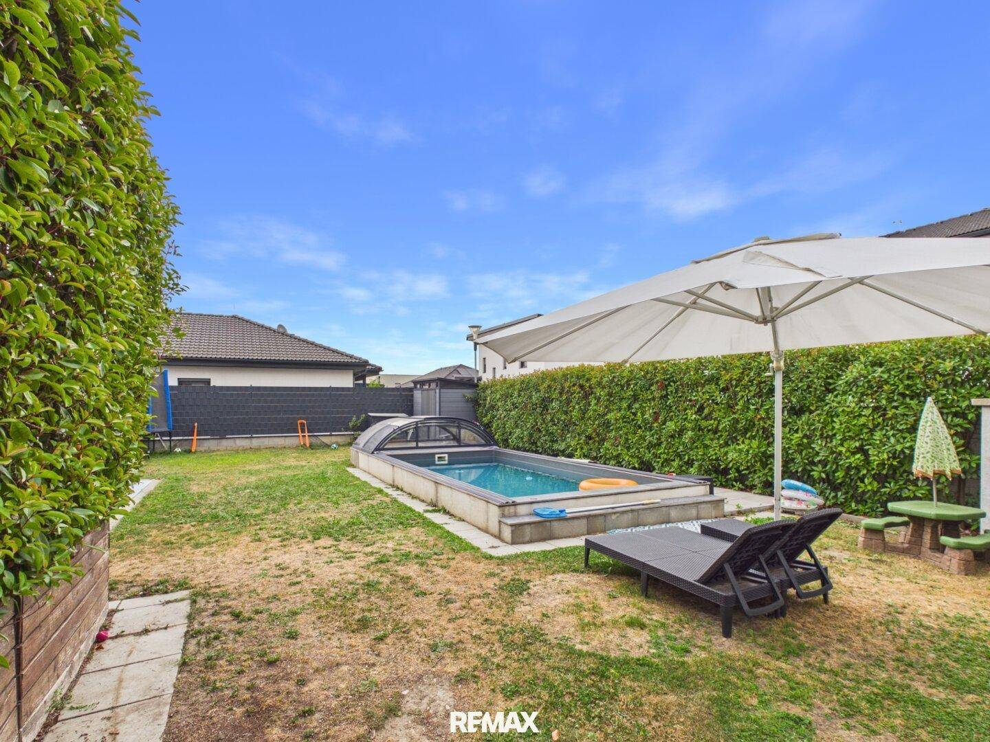 Sonniger Garten mit Pool, bequemen Liegestühlen und großem Sonnenschirm für entspannte Stunden.