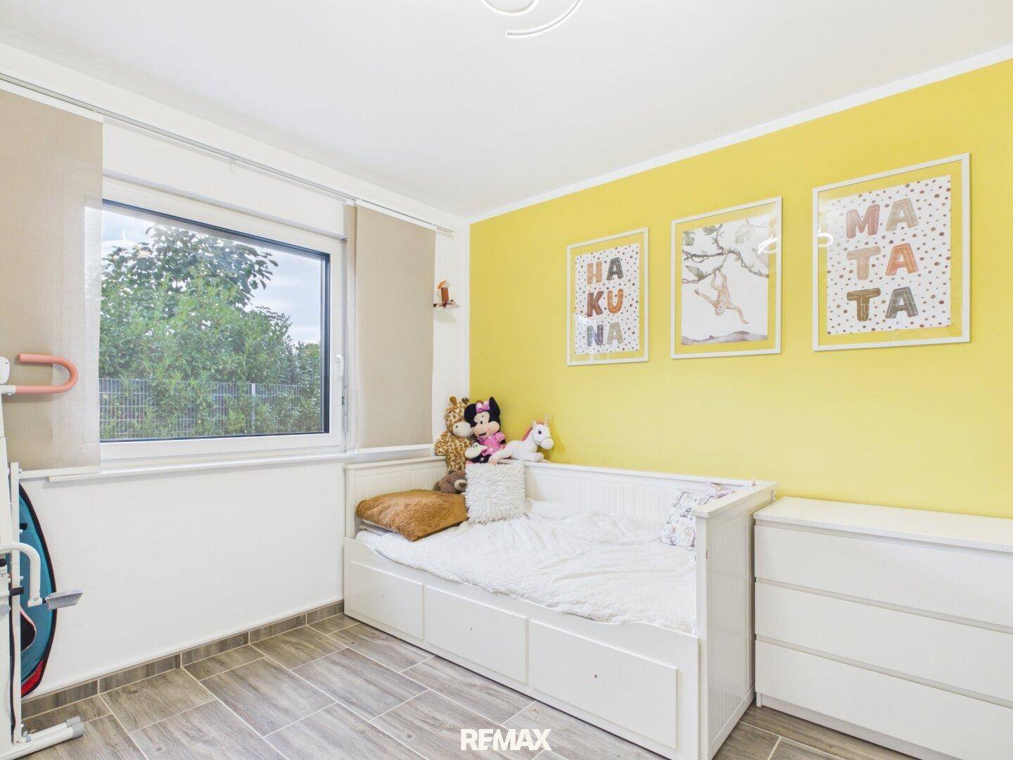 Helles Kinderzimmer mit Einzelbett, gelber Wandgestaltung und viel Tageslicht.