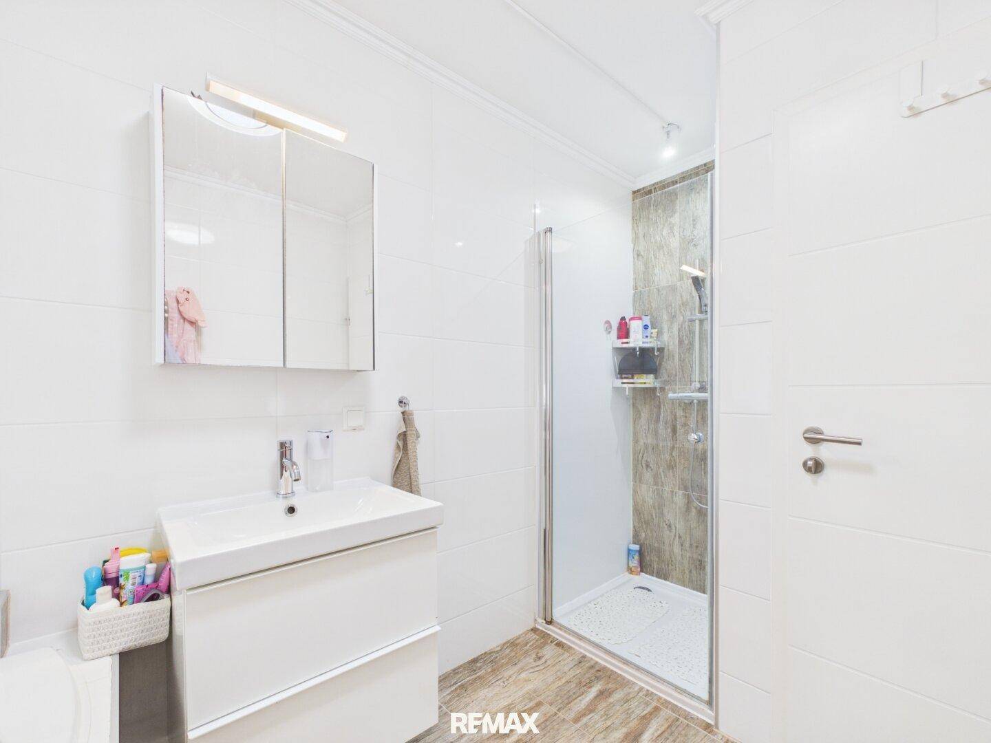 Helles Badezimmer mit Duschkabine, modernem Waschbecken und weißen Wandfliesen.