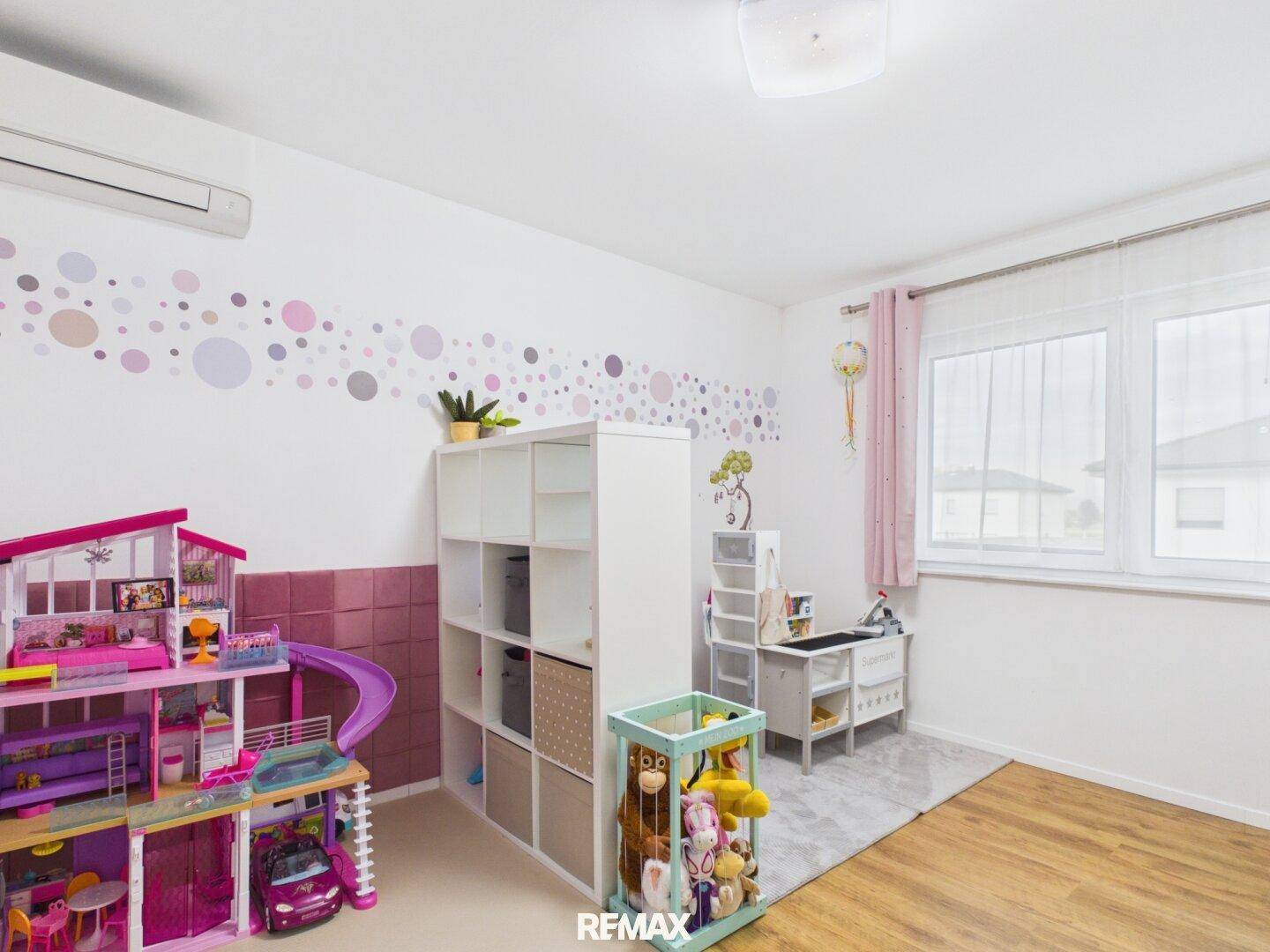 Spielzimmer mit vielen Spielsachen, Puppenhaus und farbenfroher Wanddekoration.