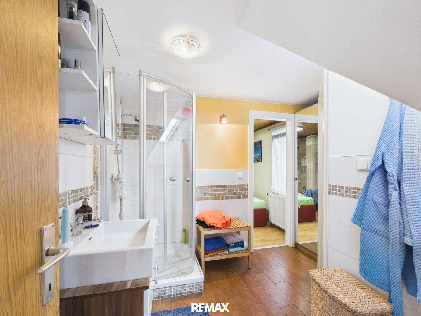 Modernes Badezimmer mit Duschkabine, Waschbecken und Holzoptik-Fliesenboden.